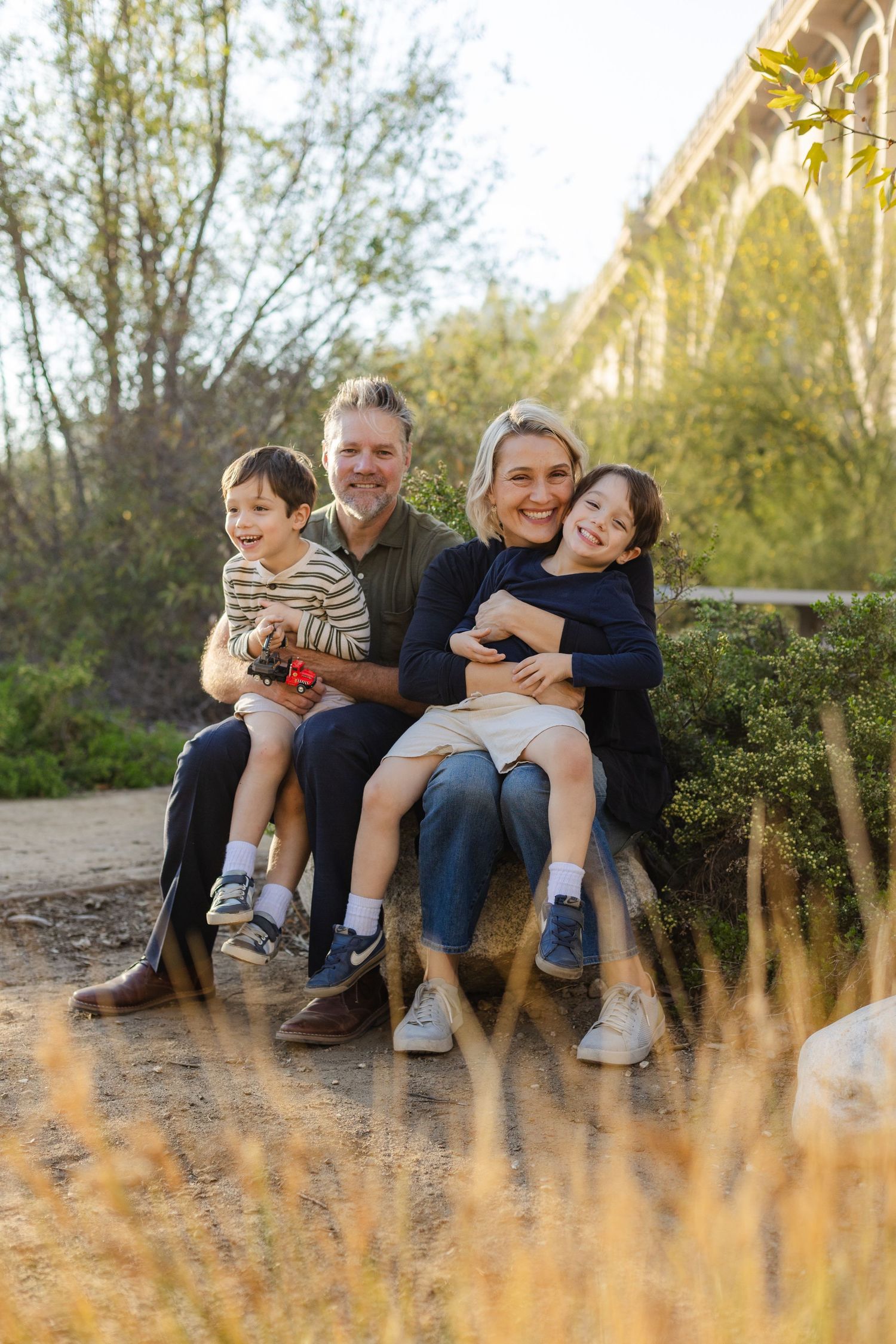 Family sitting together on rocks under a bridge during sunset photo session.