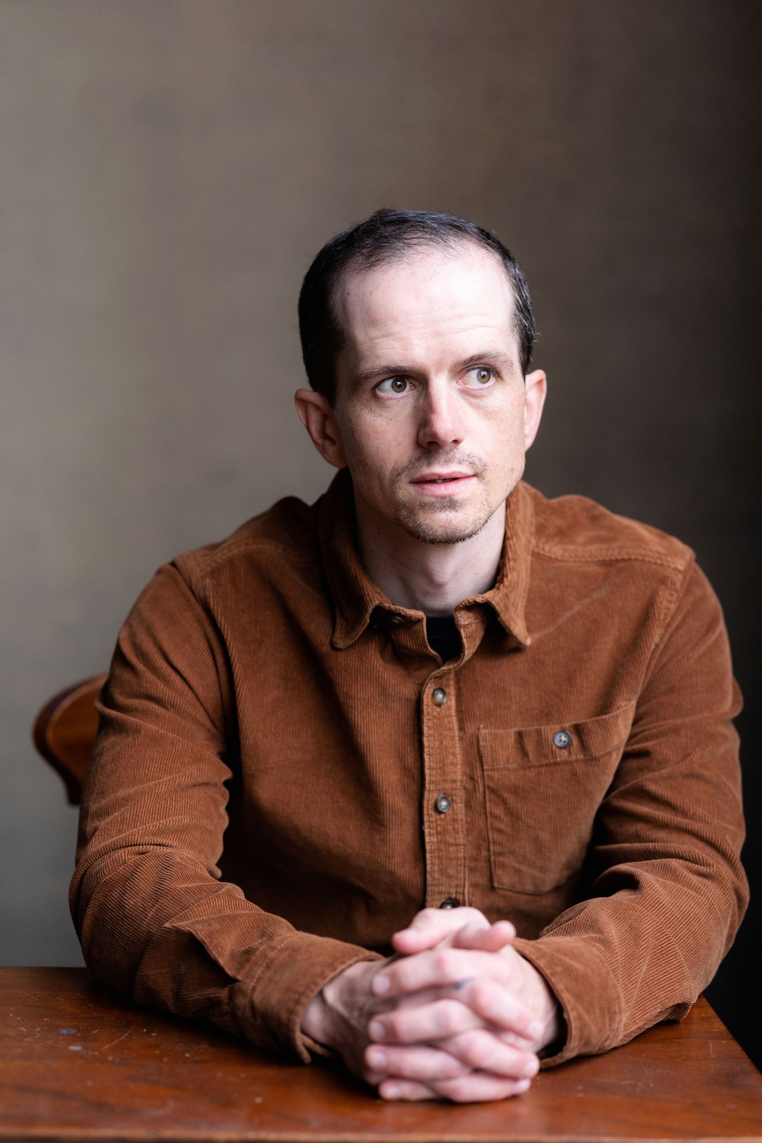 Person in brown corduroy jacket sits at wooden table in contemplative poses.