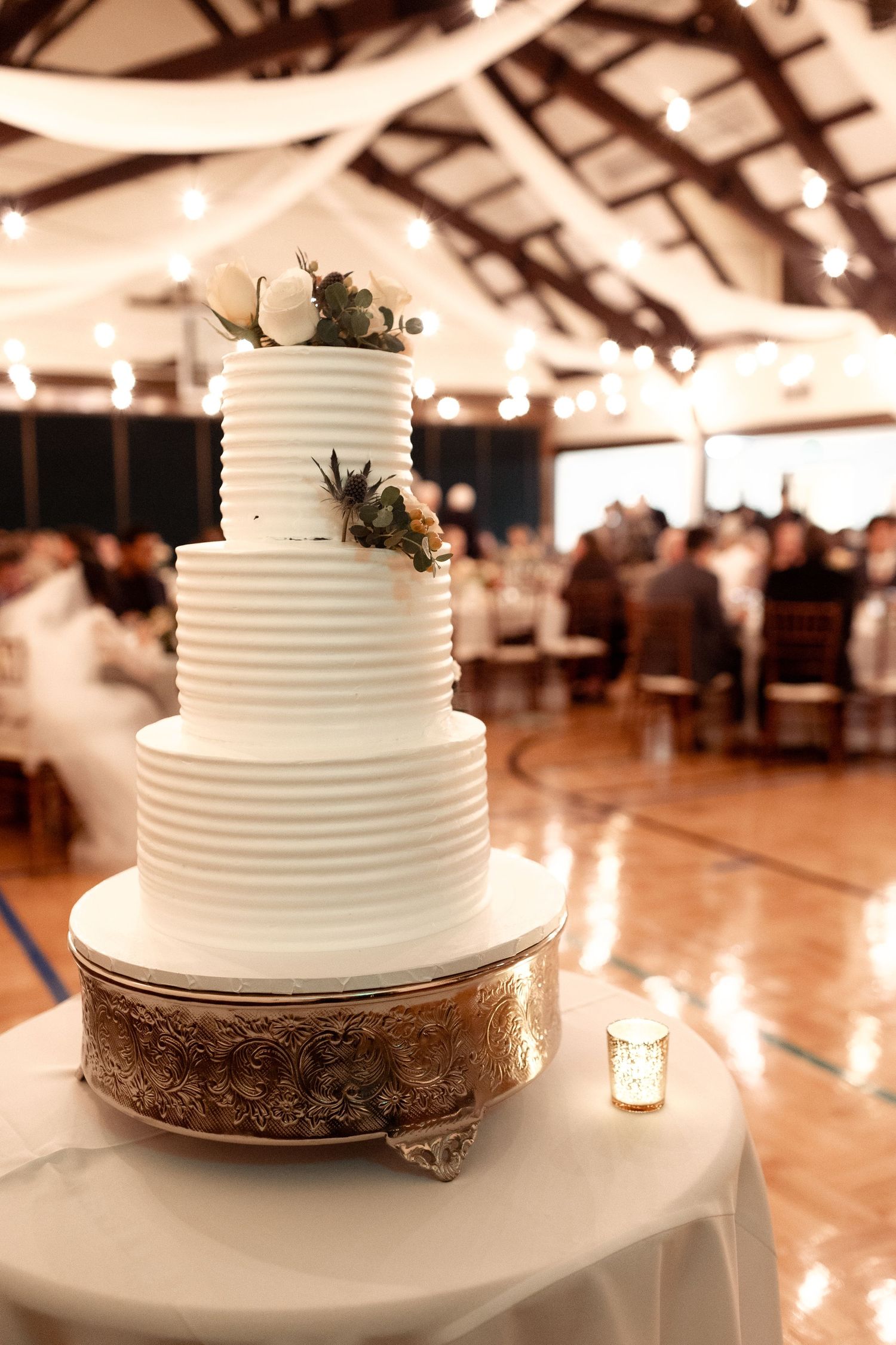 An elegant three-tiered white wedding cake with textured frosting and floral decorations in a reception venue.