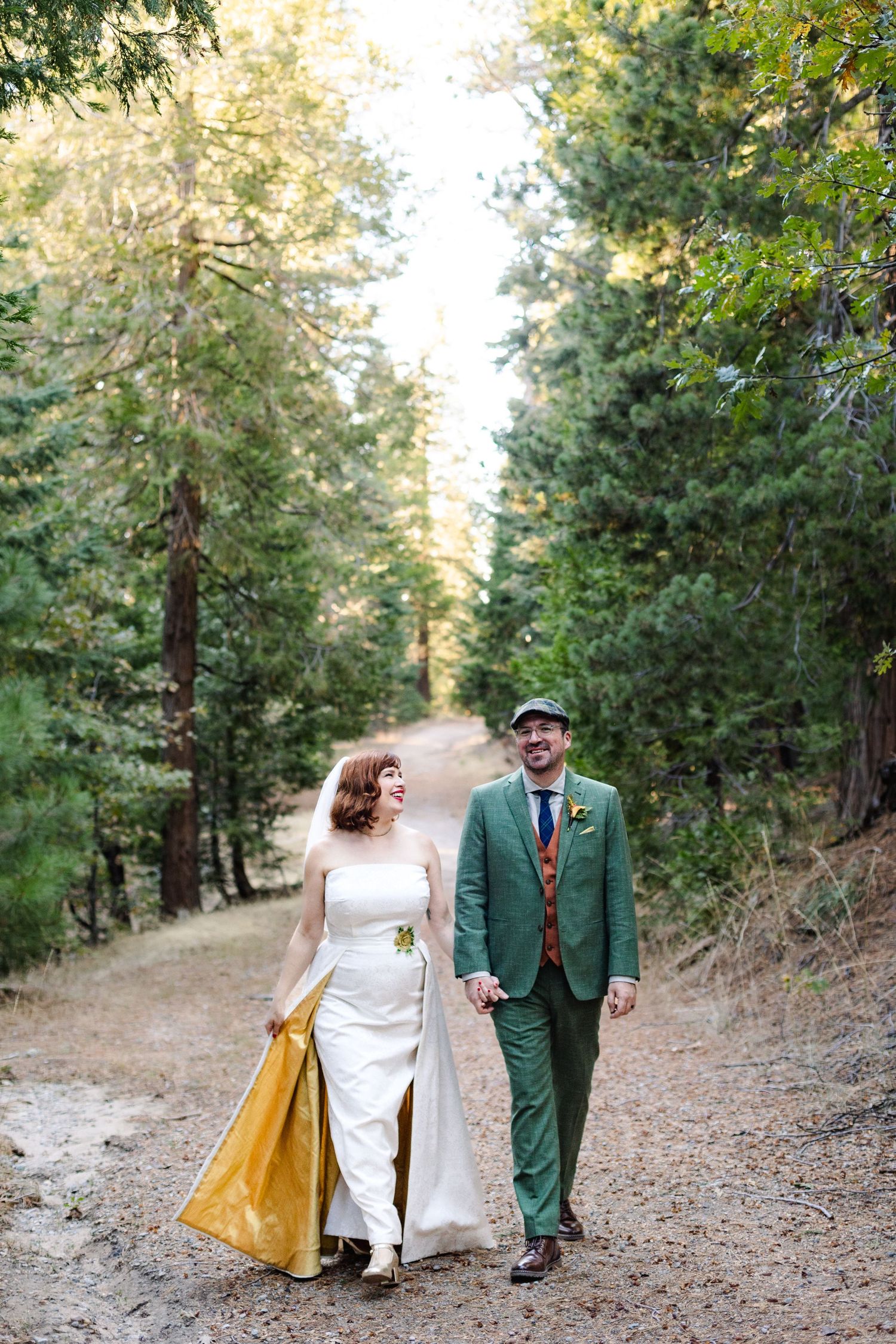 Wedding couple walking together on forest path with bride holding yellow cape.