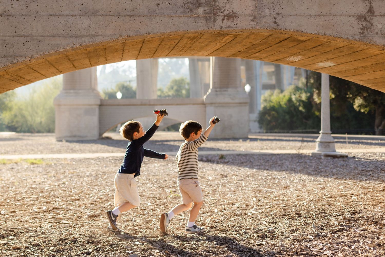 Children playing and running under a concrete bridge structure.