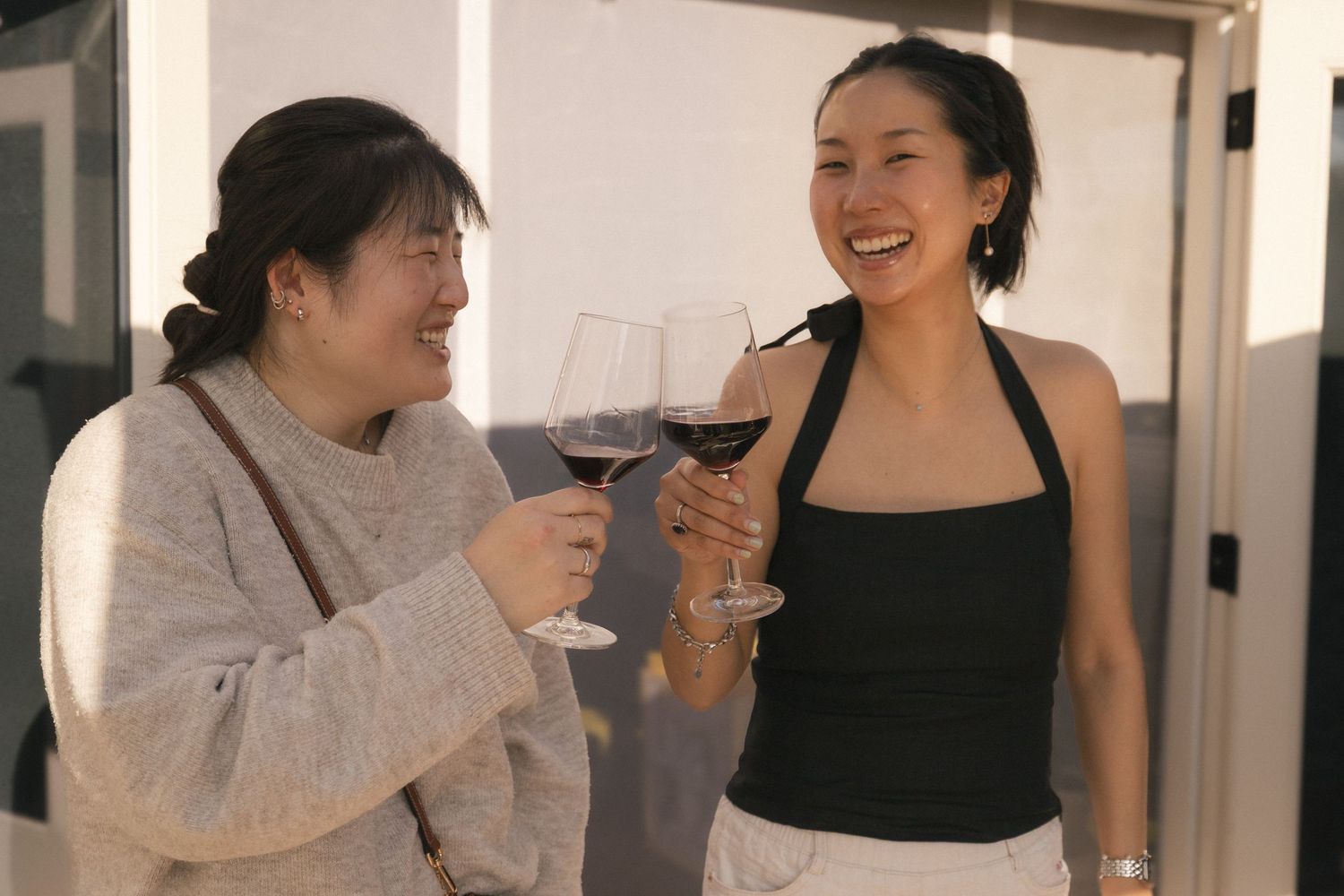 Two women smiling and toasting with glasses of red wine at an outdoor gathering.