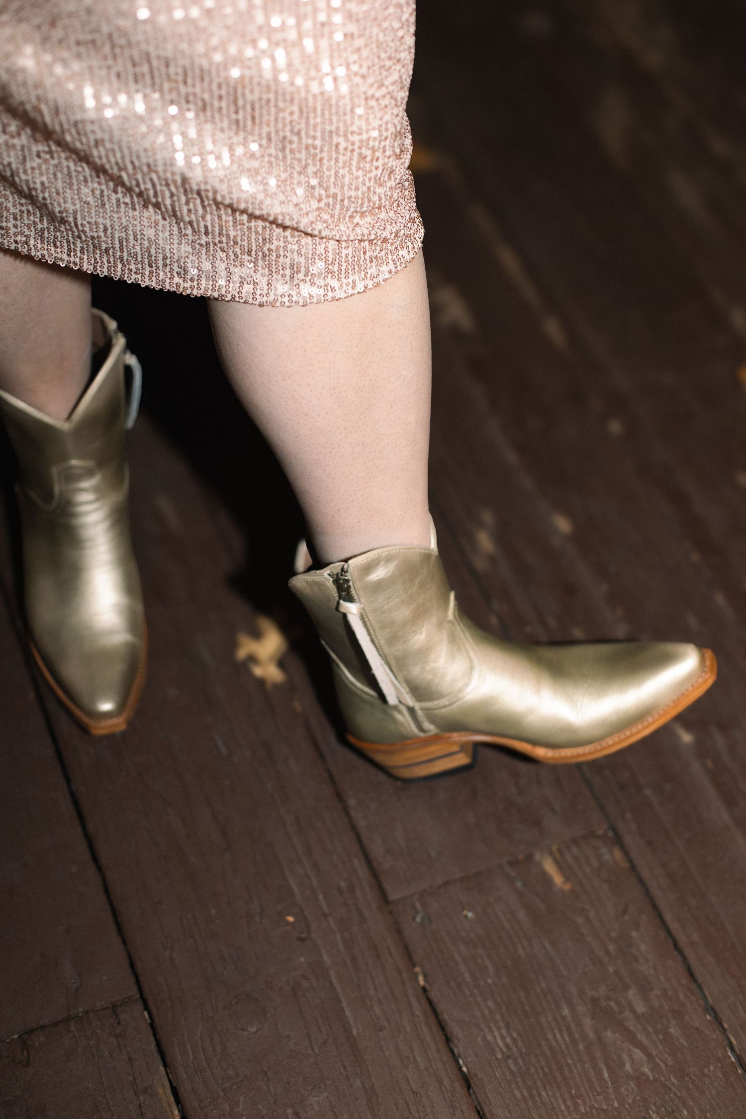 Close-up sequence of metallic gold boots on dark wooden floor.
