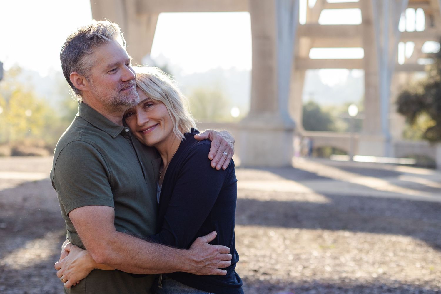 A tender embrace between a couple in casual attire standing outdoors under architectural columns.
