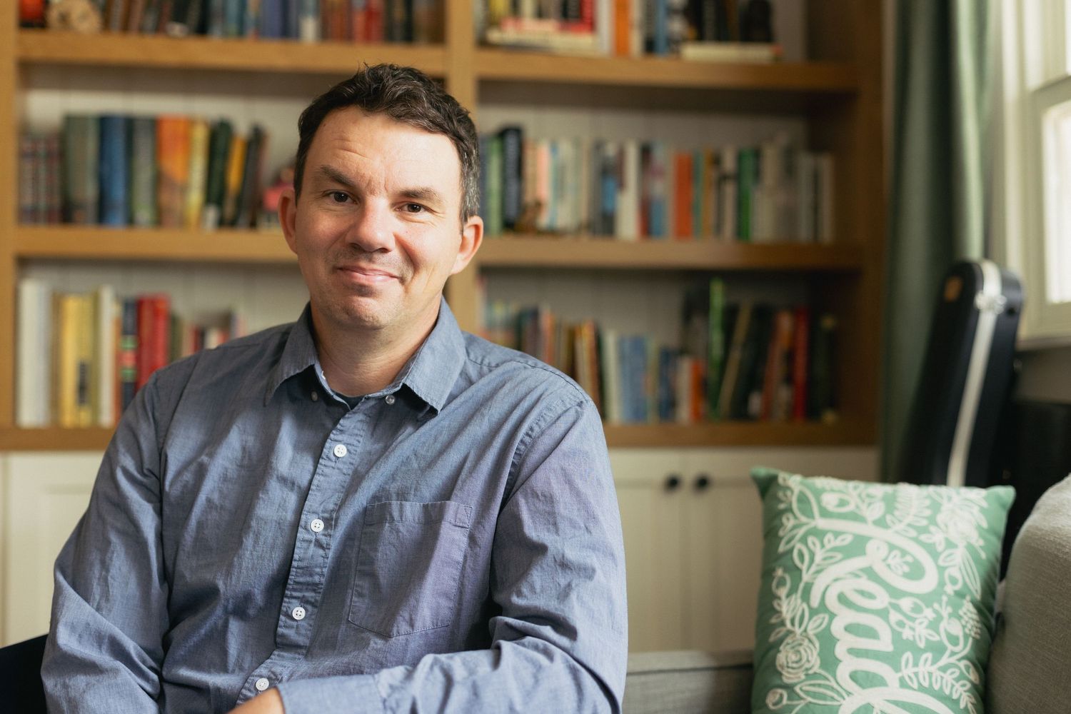 Person in blue button-down shirt sitting in front of a bookshelf.