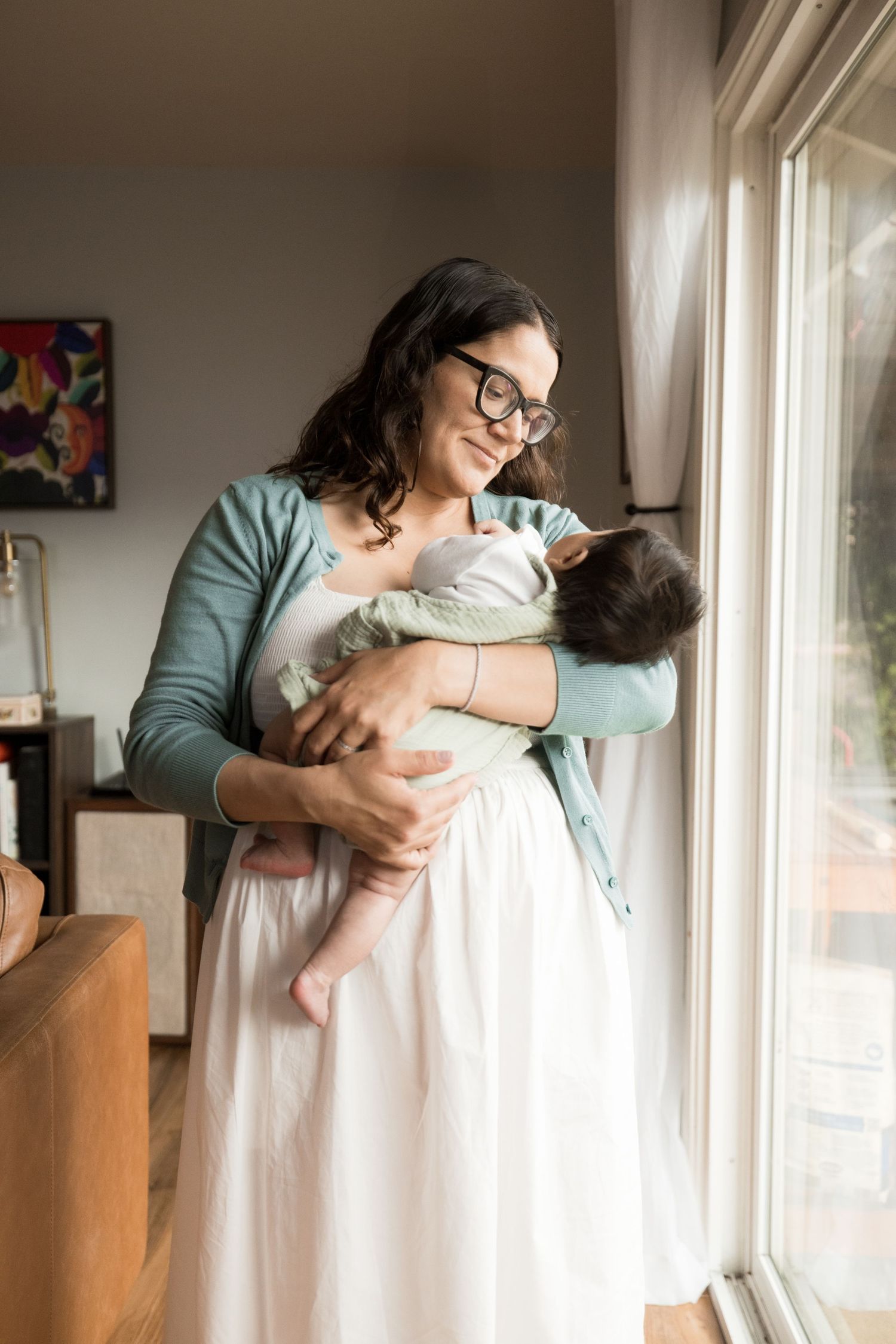 Indoor lifestyle newborn session by window light in soft muted tones.