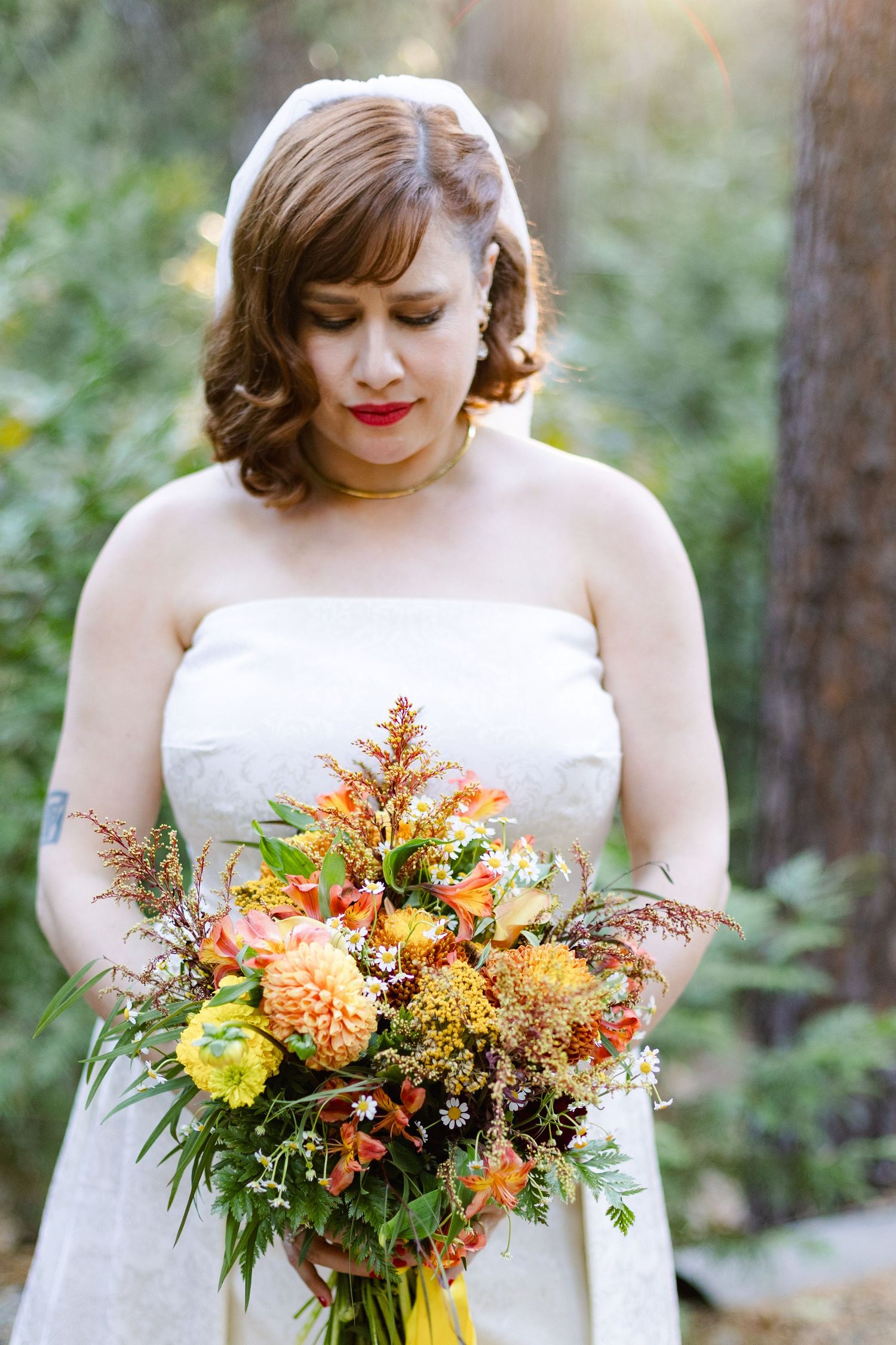 Bride holding vibrant fall-colored wedding bouquet with orange and yellow flowers.