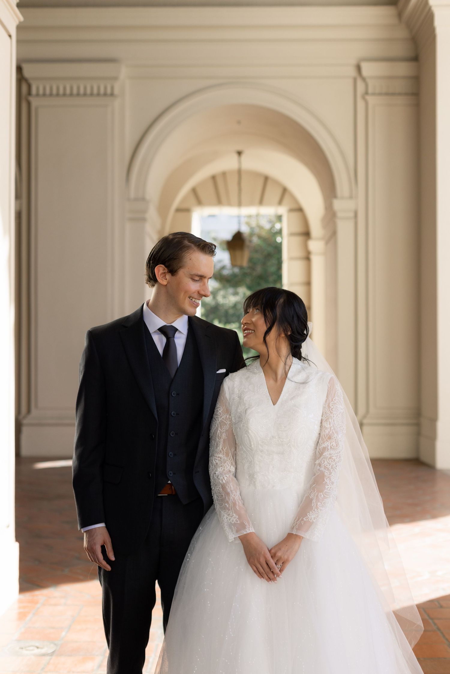 Elegant wedding couple posing in a classical colonnade with arched architecture.