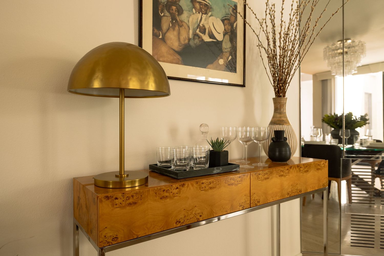 Gold dome lamp and burl wood console table with decorative vases and glassware in an elegant entryway.