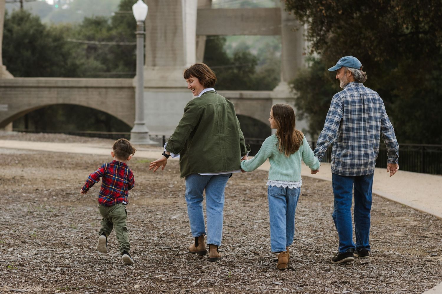 Family walking together on gravel path near stone bridge structure.