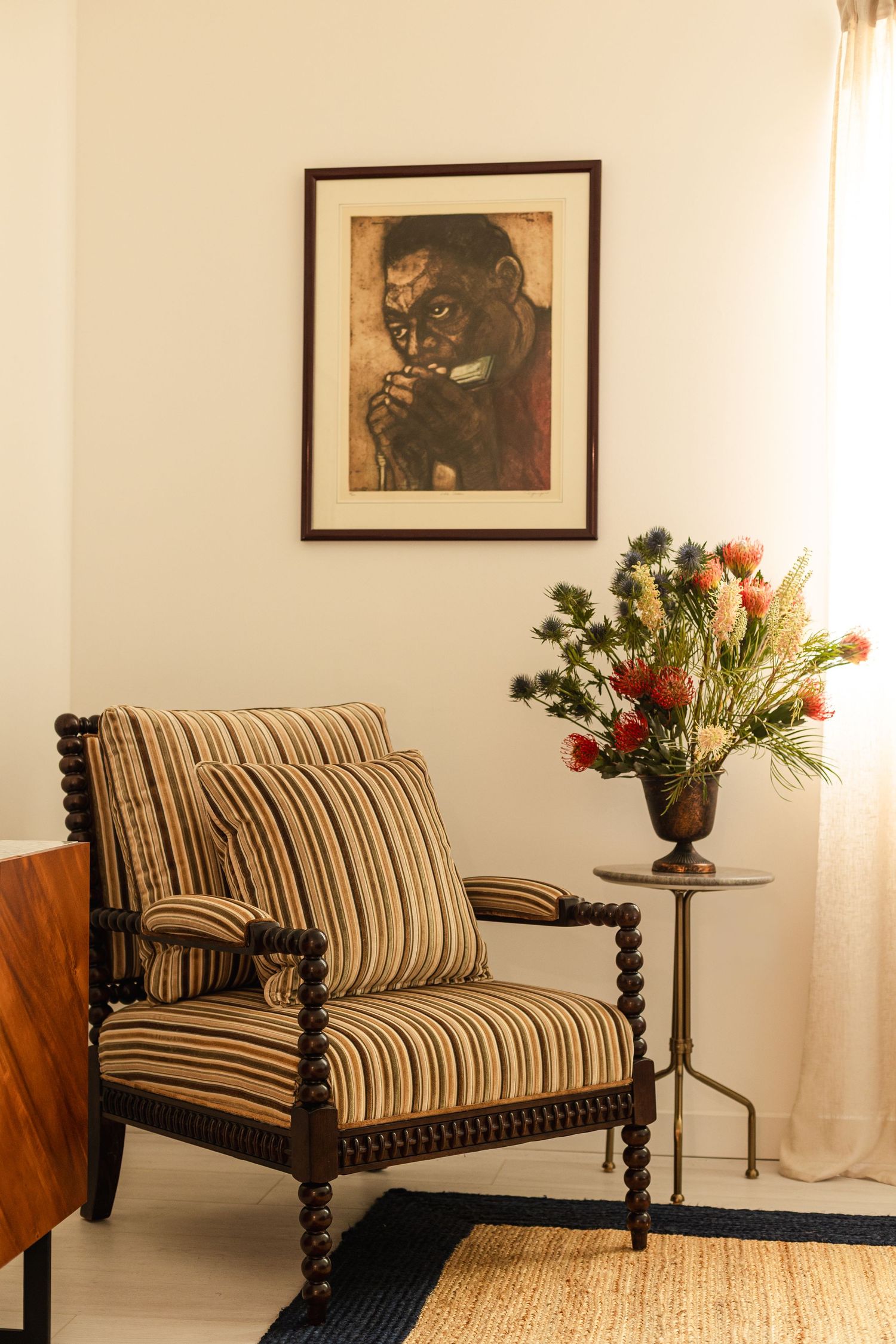 Striped armchair with bobbin legs beside a floral arrangement under a framed portrait painting.
