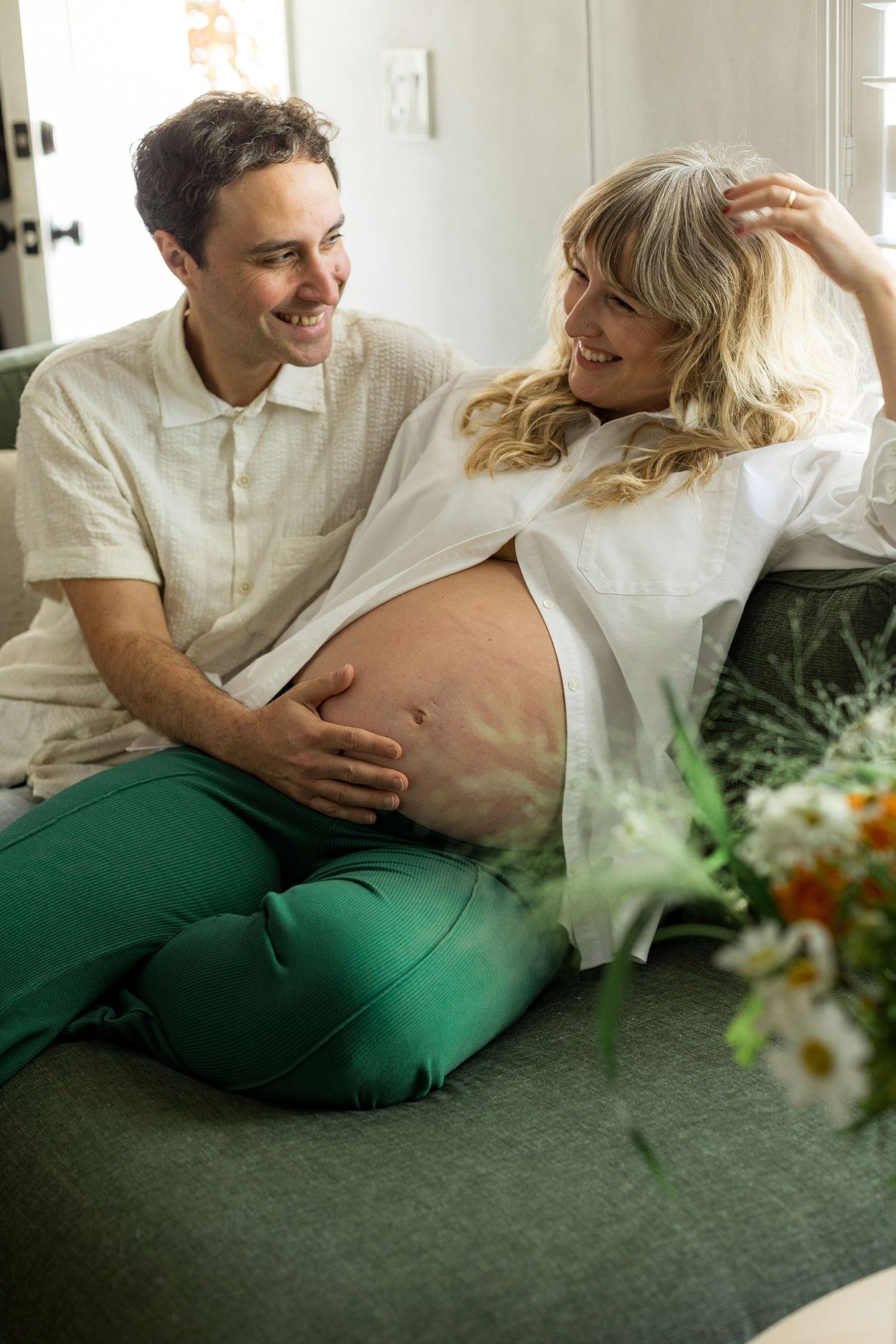 Indoor maternity session with soft lighting and floral accents on a green couch.