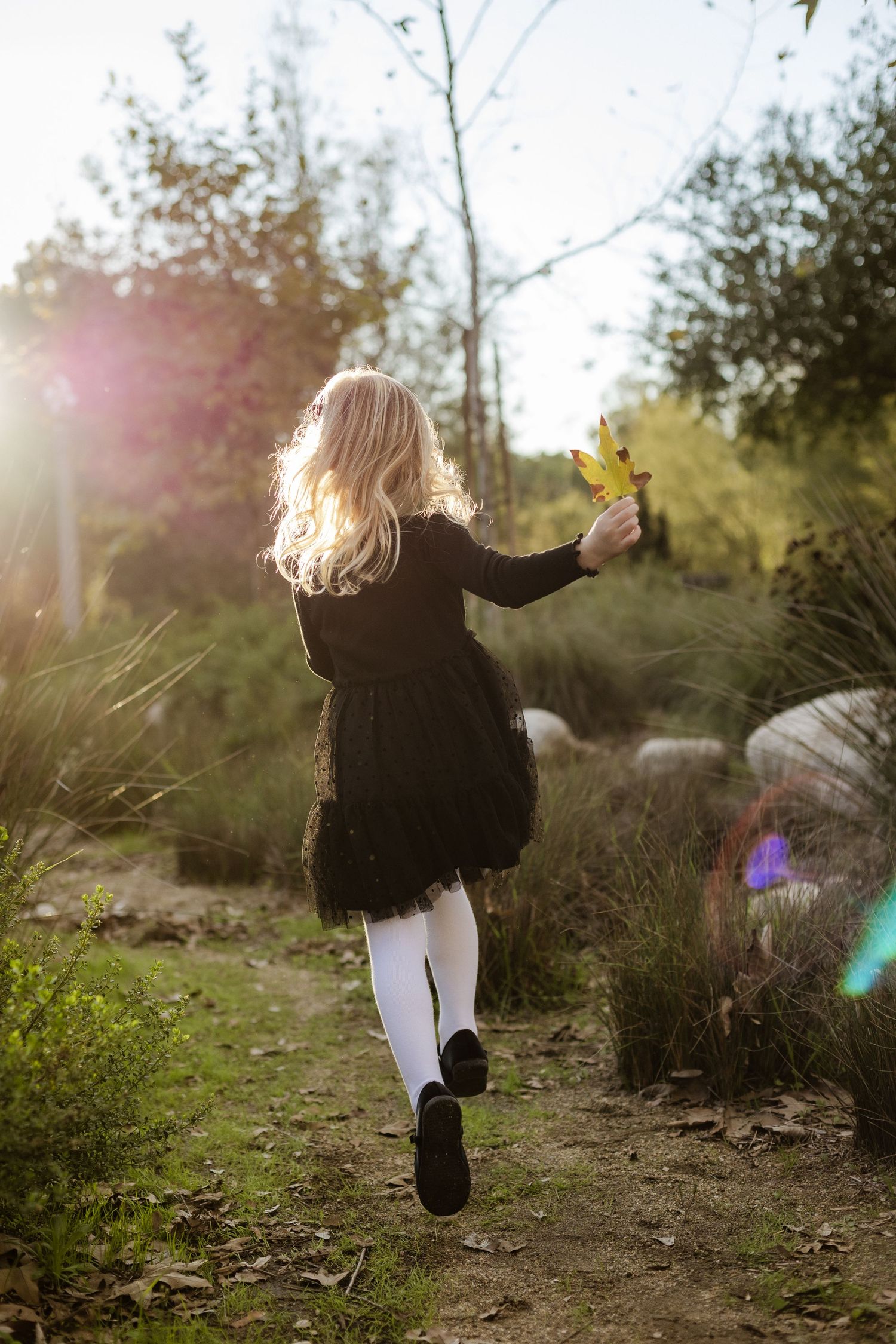 Child in black outfit running through nature trail during golden hour.