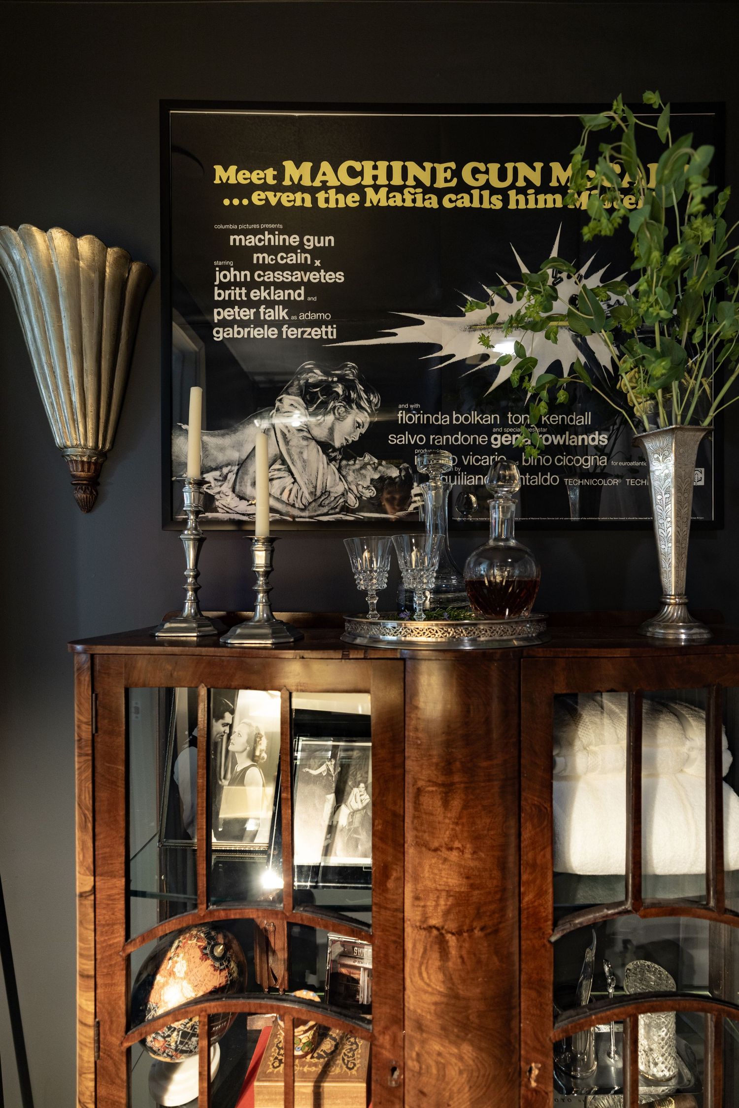 Dark vintage display cabinet with candles, crystal glasses, and movie poster above.