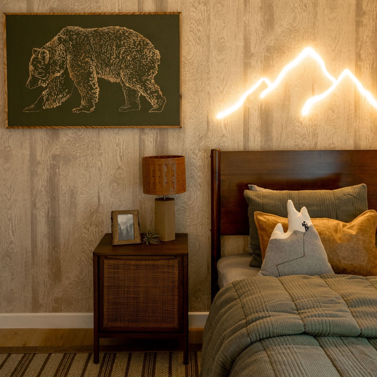 Cozy boys bedroom with bear wall art, neon mountain light, plaid bedding, and wooden nightstand.