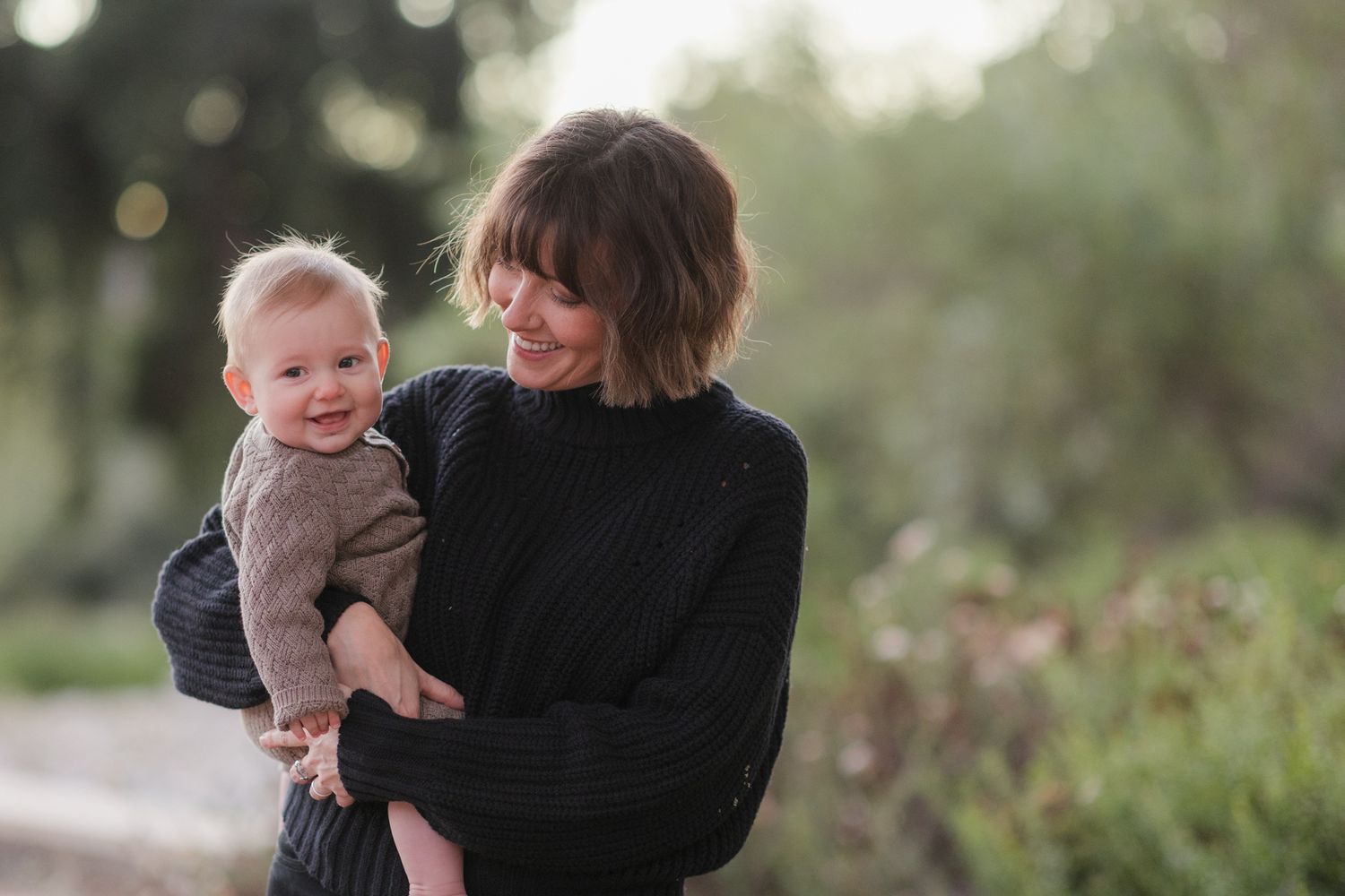 Family photoshoot in a natural outdoor setting during golden hour with warm sunlight filtering through.