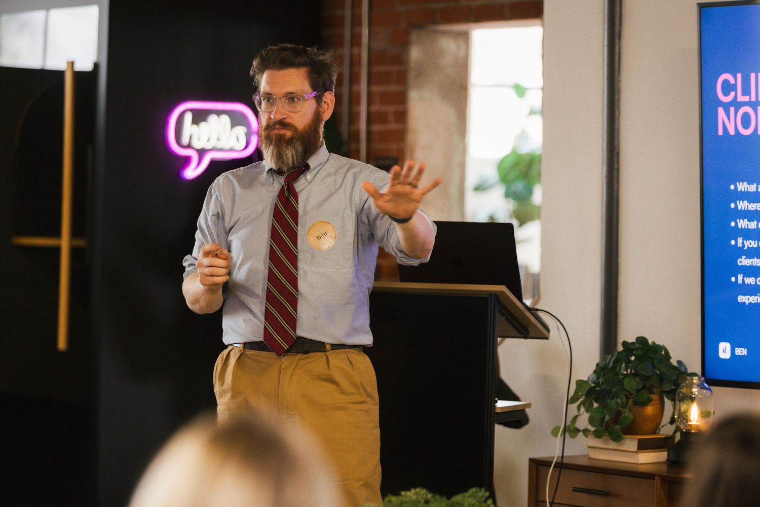 Professional speaker presenting to an audience in a modern office space while holding papers and gesturing.