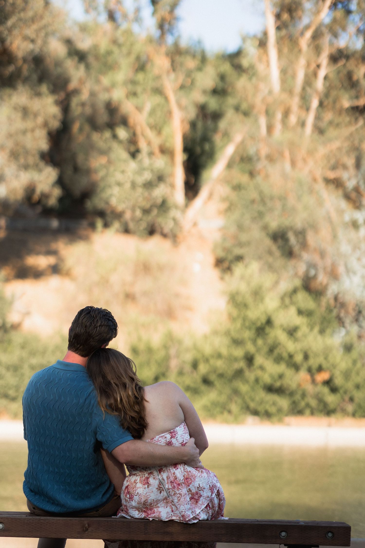 A couple sits close together on a bench overlooking a peaceful lake view.