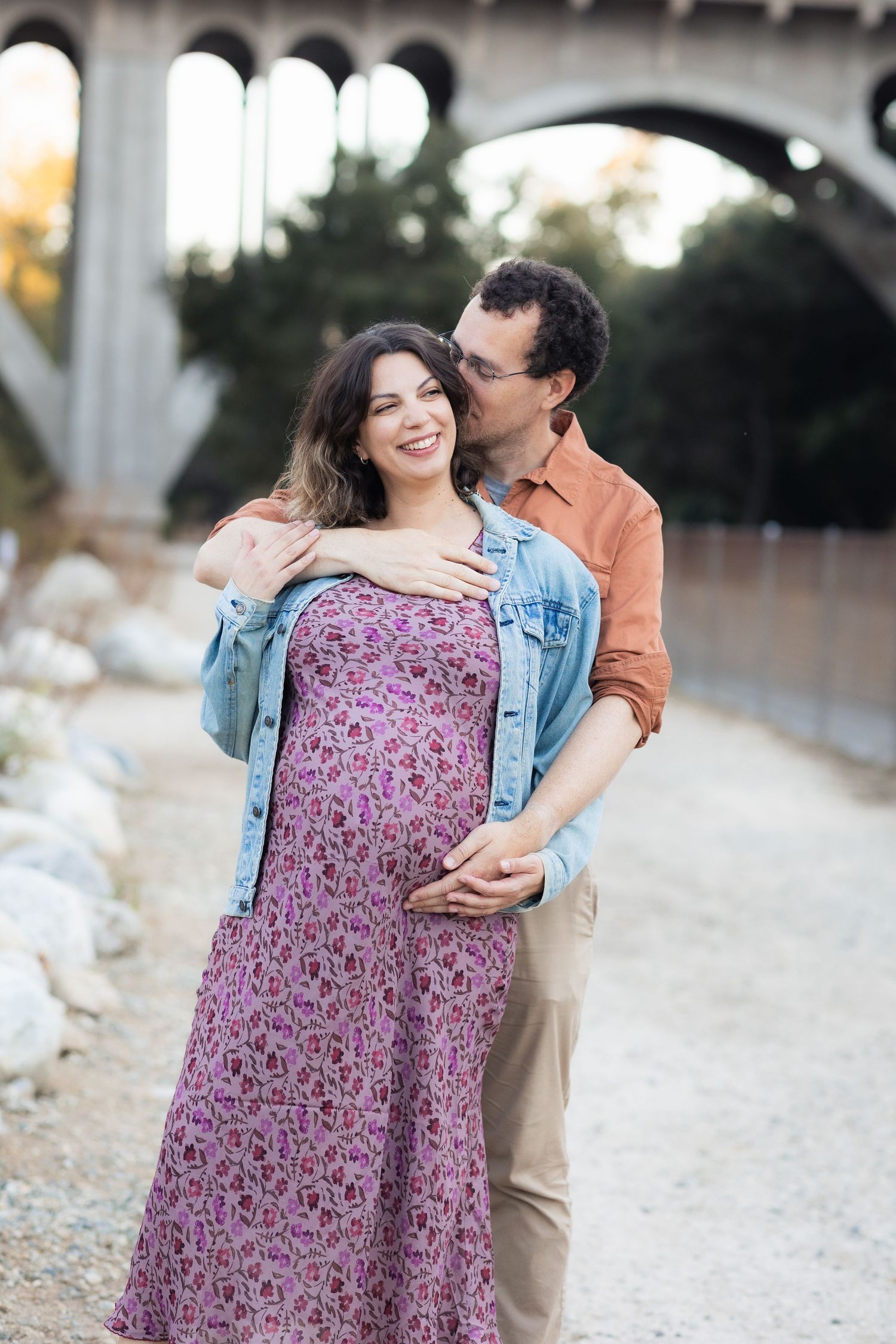 Romantic maternity photoshoot under stone bridge during golden hour.