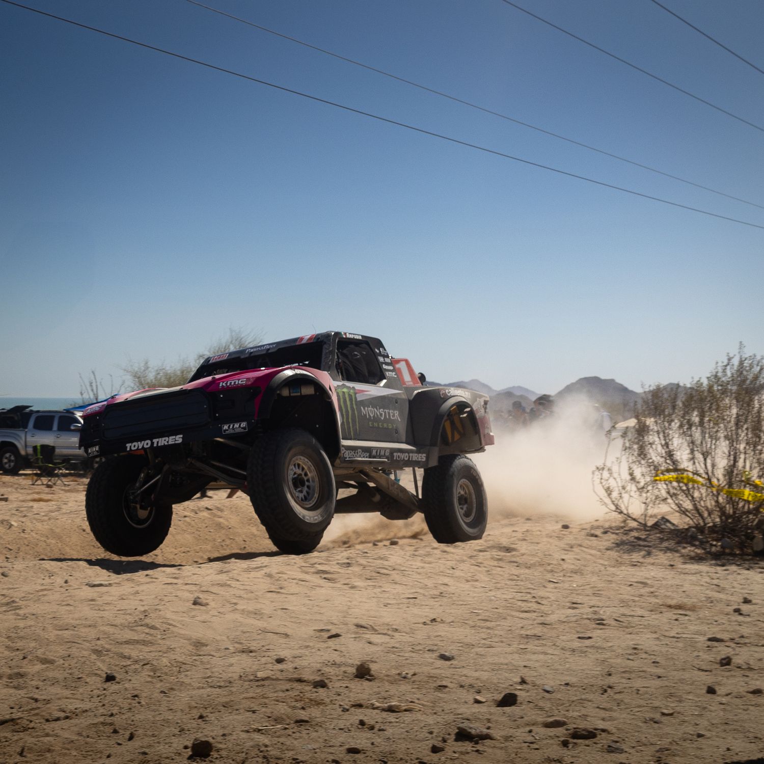 “Monster Energy Trophy Truck speeding through a sandy Baja desert wash at the San Felipe 250, trailing a dust cloud.”