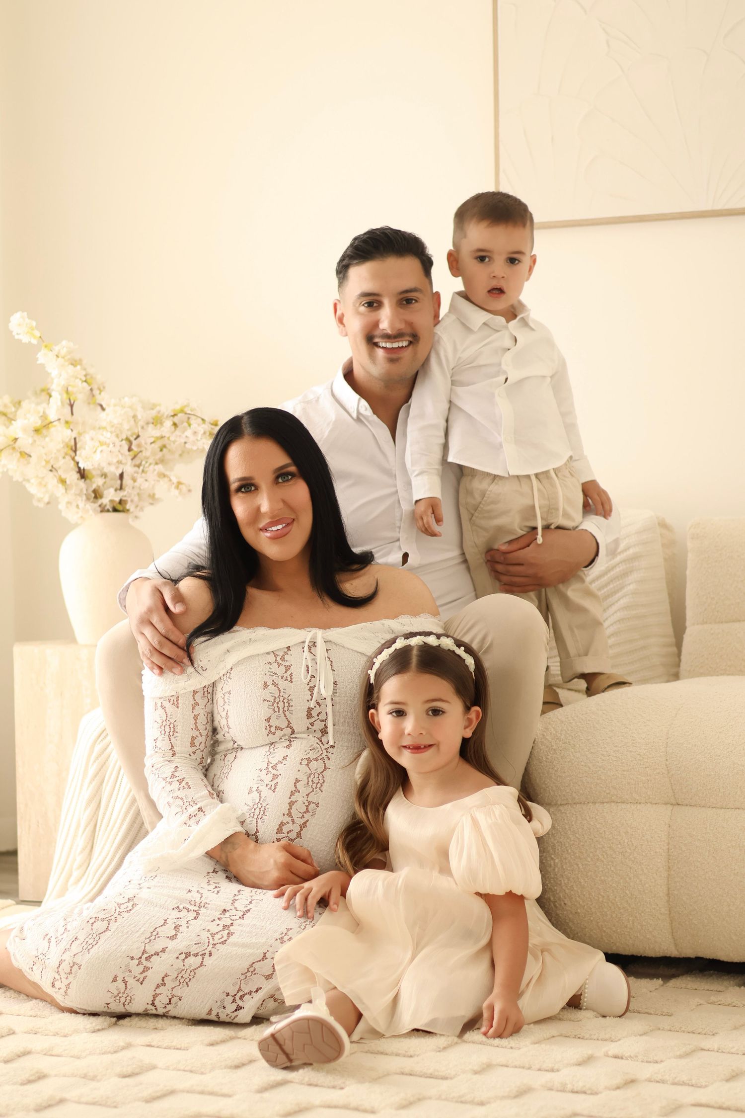 Maternity photography portrait of family sitting together in a dreamy studio with creamy white aesthetic