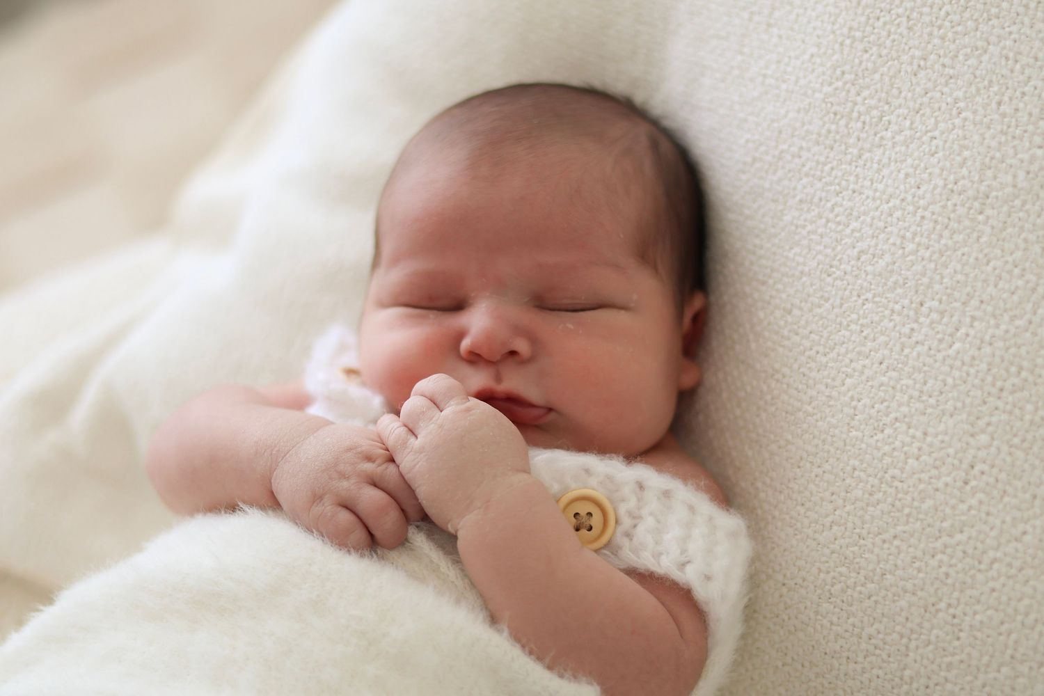 Newborn photography portrait of a sleeping baby wrapped in a soft beige blanket on a fuzzy rug