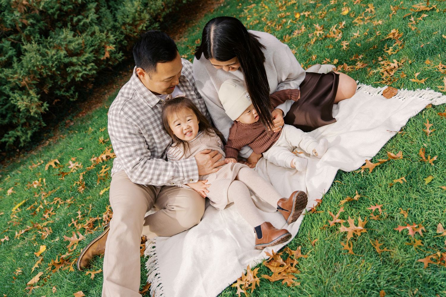 Family relaxing together on picnic blanket surrounded by fallen autumn leaves.