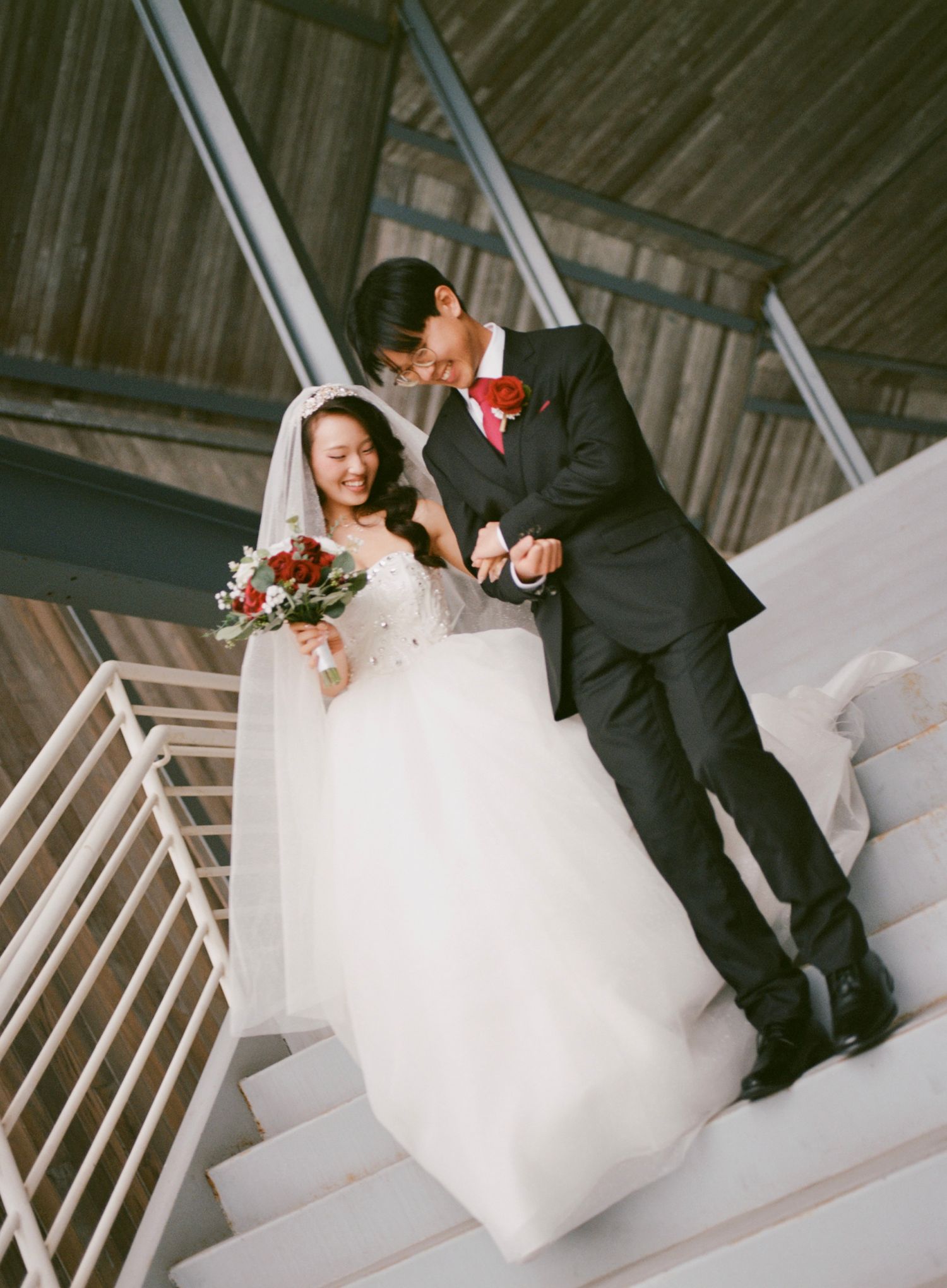 Newlyweds sitting together on white stairs in formal attire.