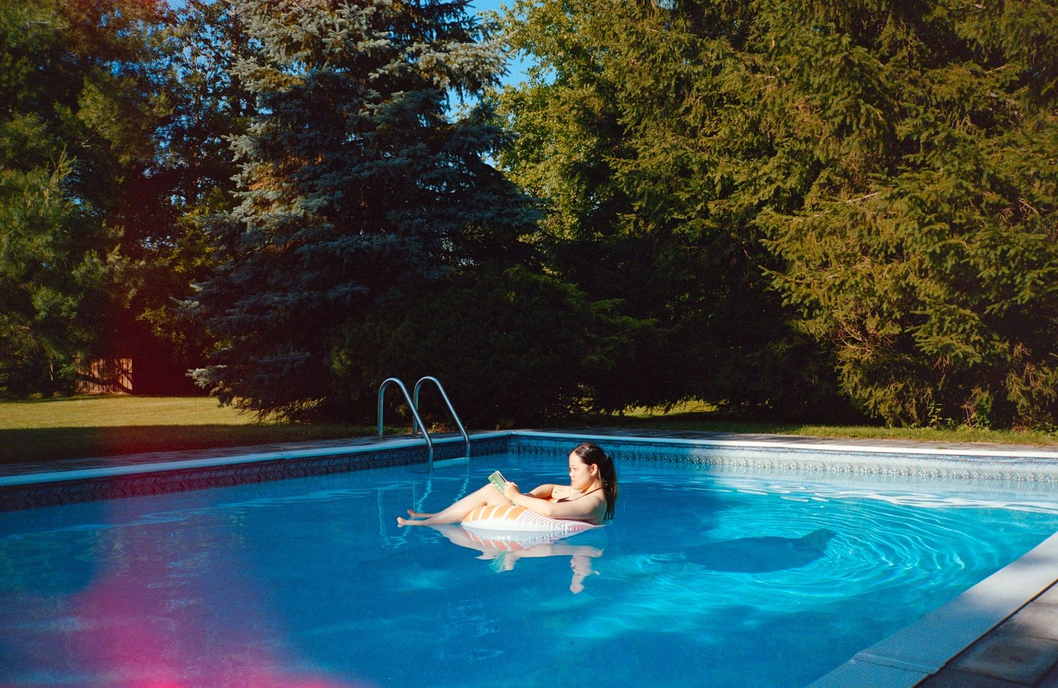 A person performs an acrobatic flip sequence into a backyard swimming pool on a sunny summer day.