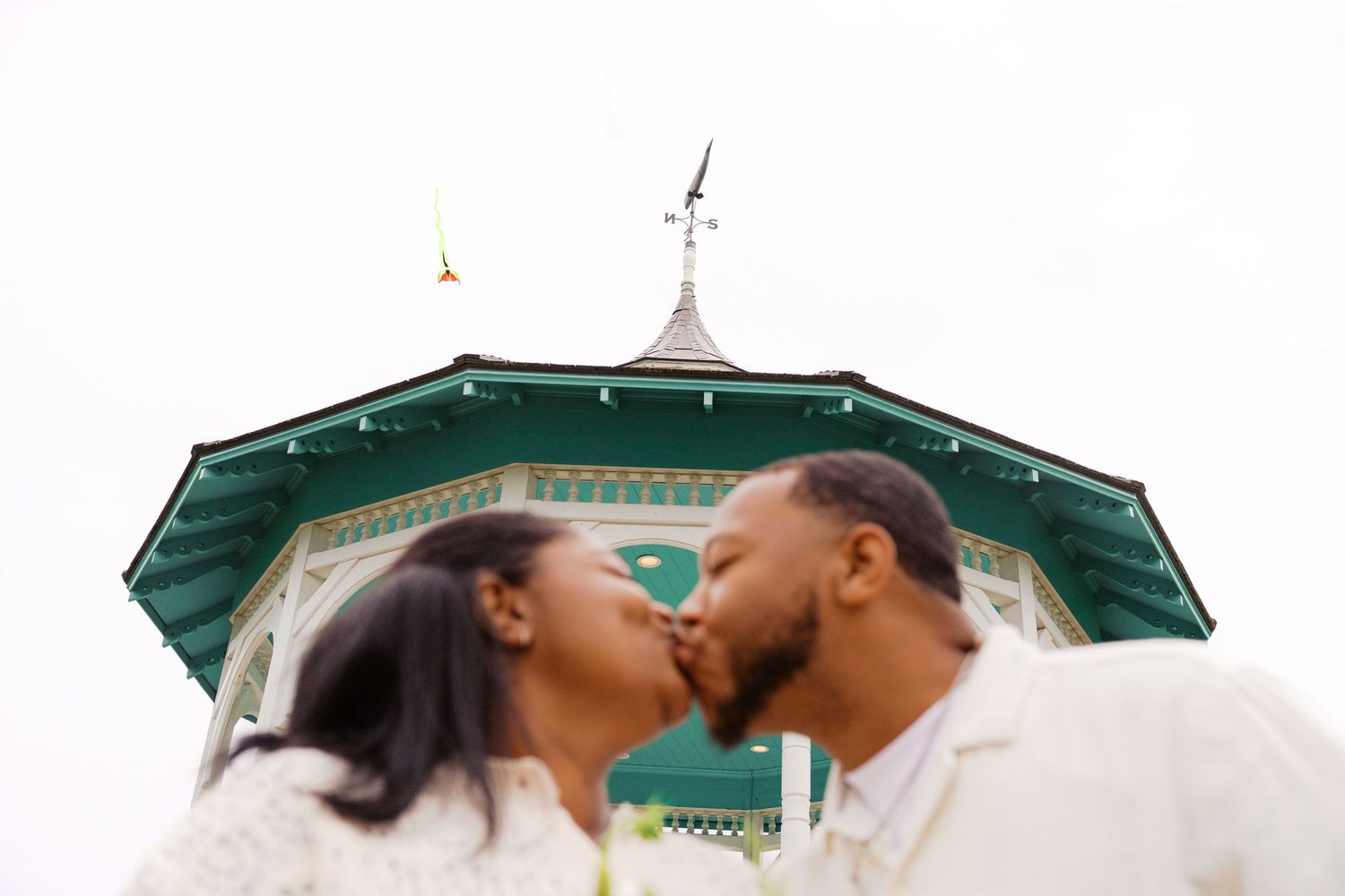 A romantic kiss under a decorative white gazebo on a sunny day.