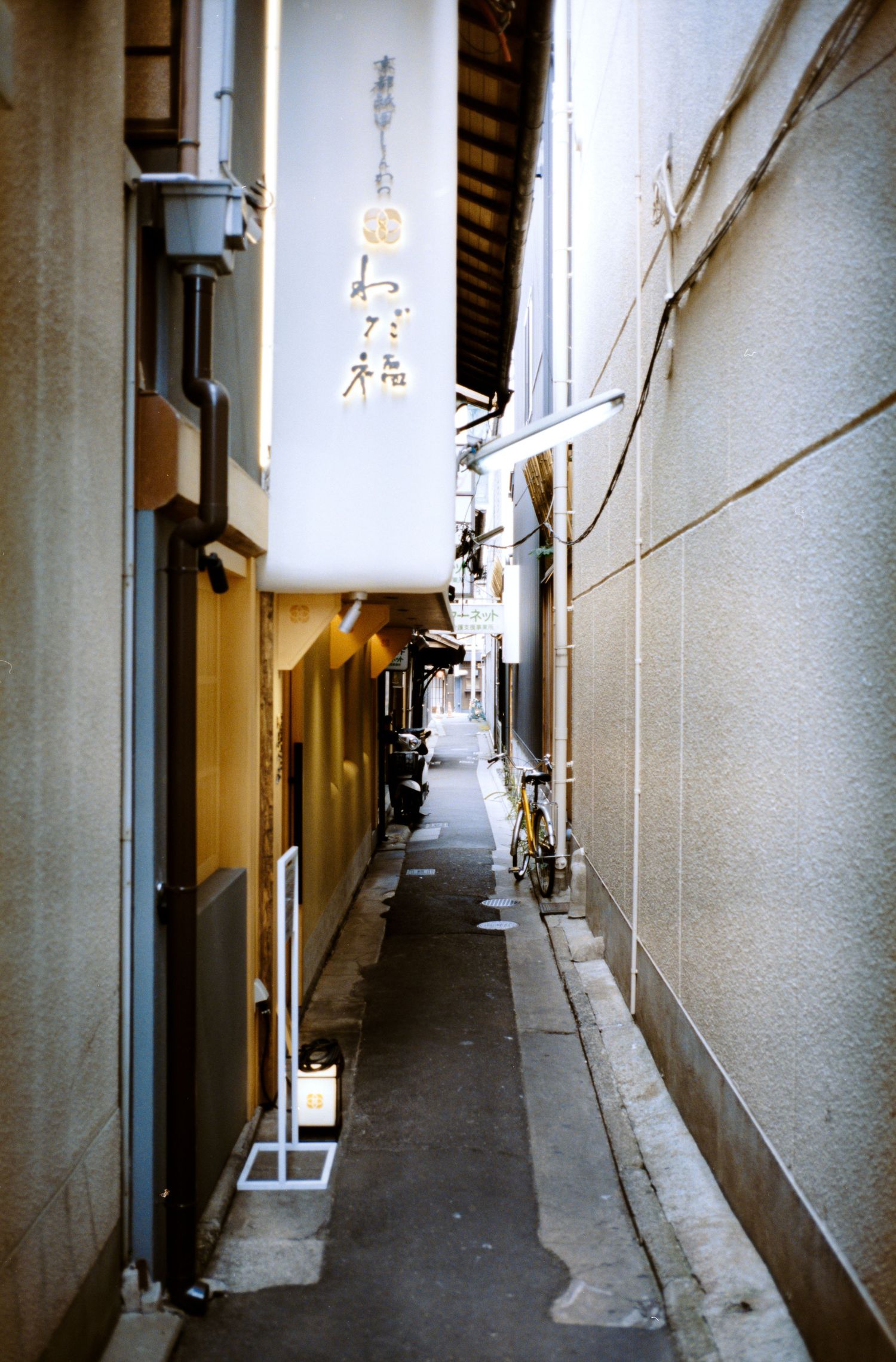 A narrow alley between buildings with Japanese text on banners and traditional architecture.