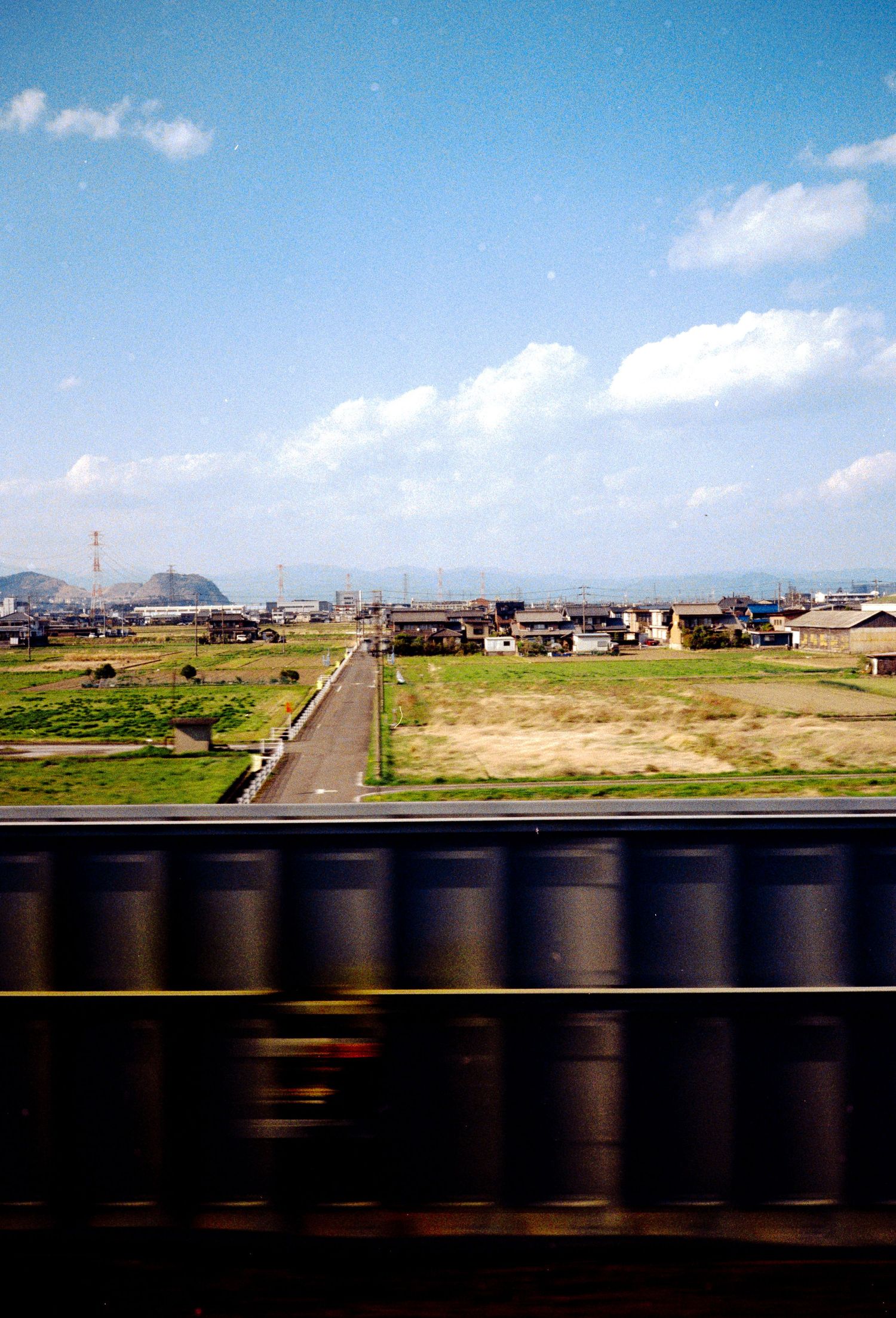 Panoramic view of Japanese countryside with houses and fields seen from a moving train.