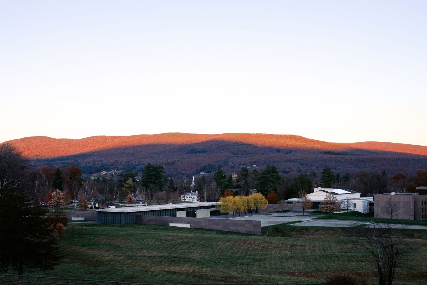 A row of modern desert houses with white exteriors and large windows set against a backdrop of red mountains at sunset.
