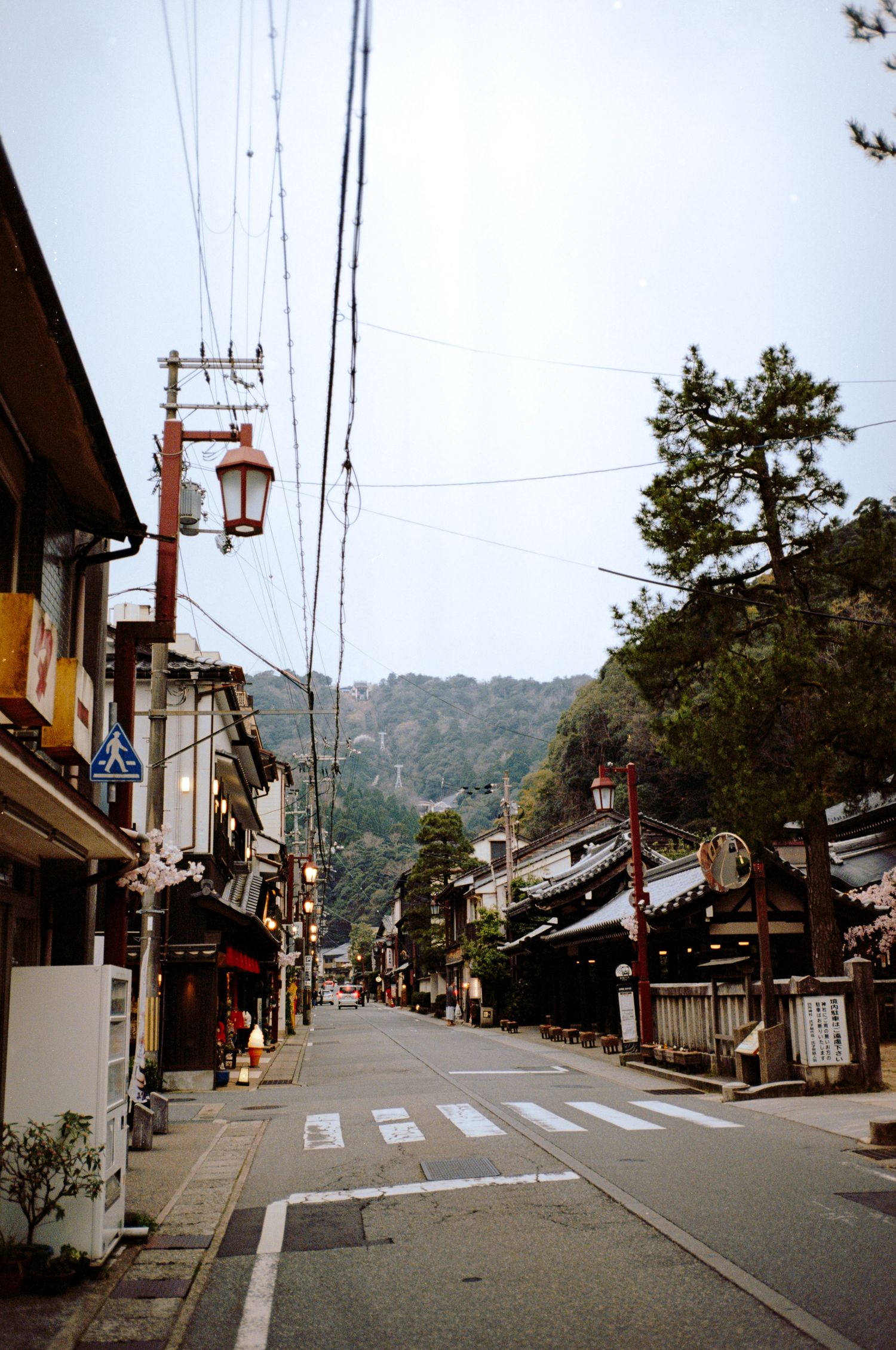 A traditional Japanese shopping street with lanterns and historic architecture leading to mountain views.