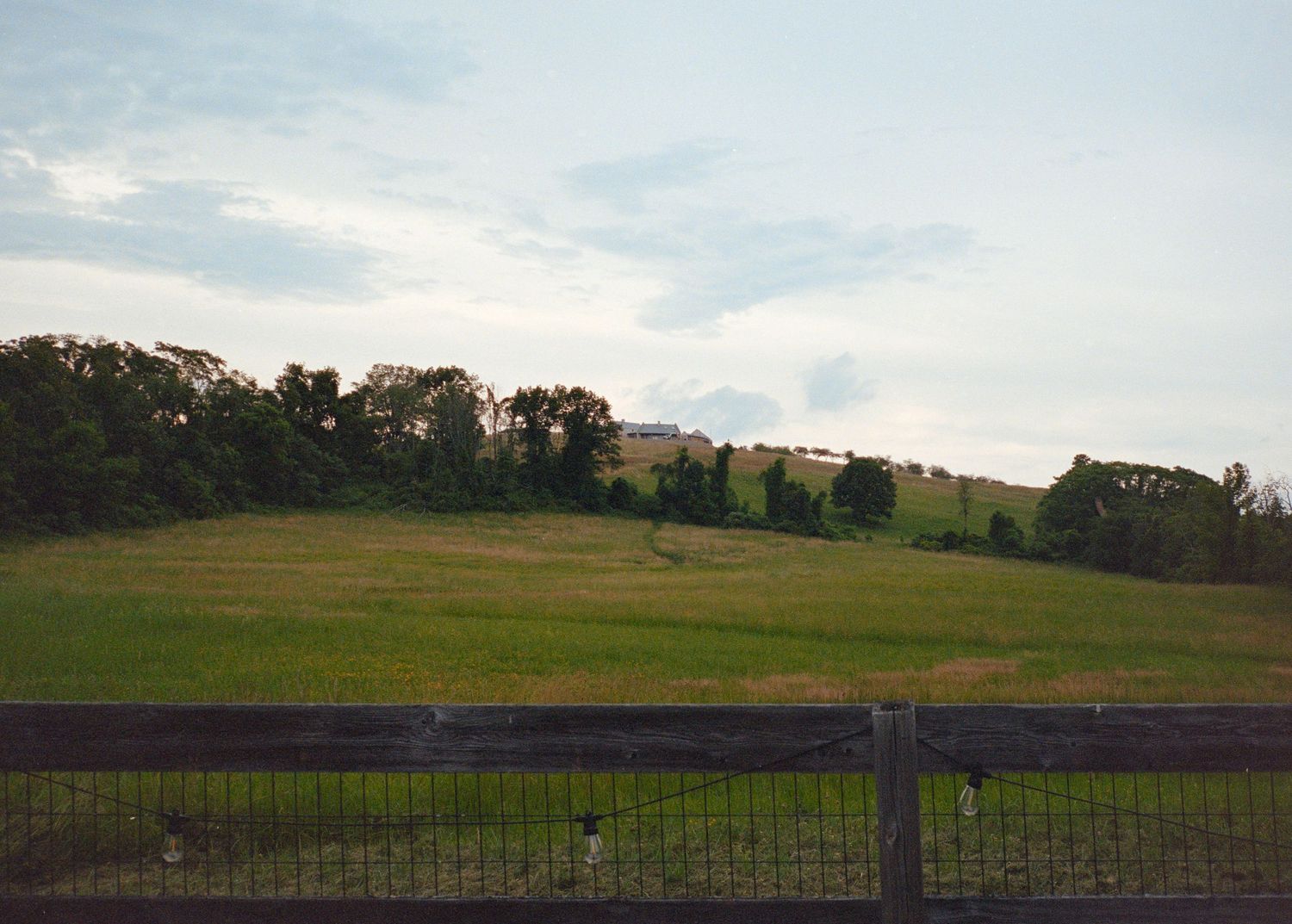 A panoramic view of rolling green hills and farmland stretches across the horizon under a cloudy evening sky.