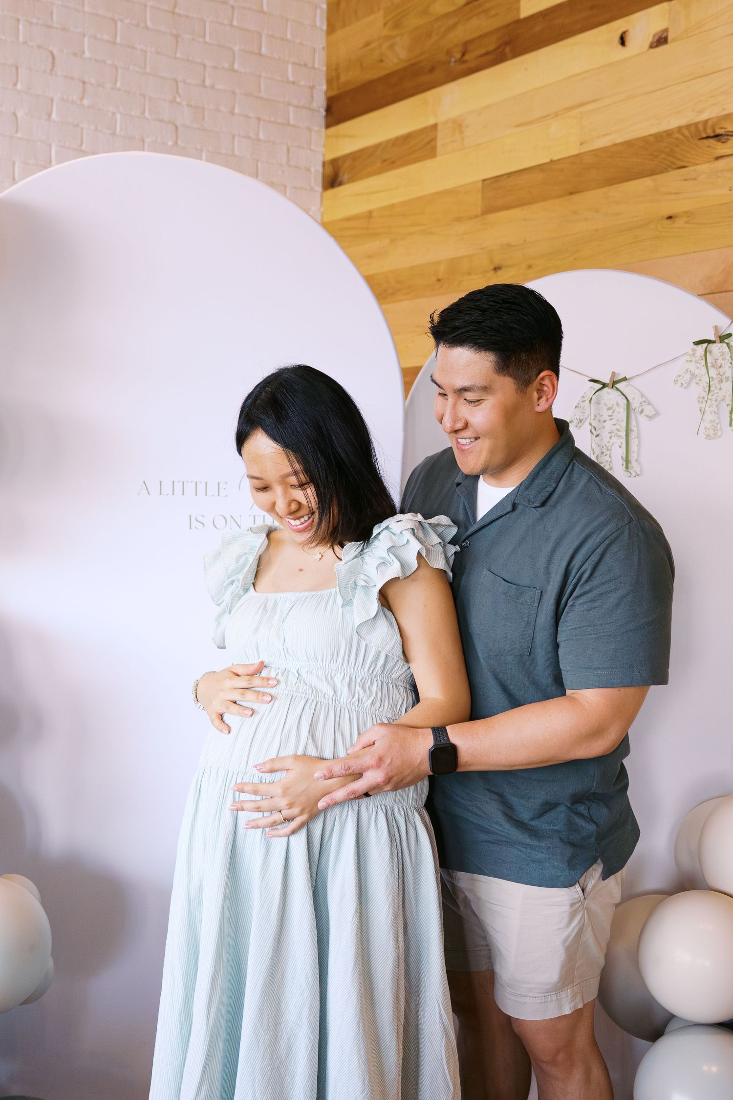 Couple shares tender moment against white brick wall during maternity photoshoot.