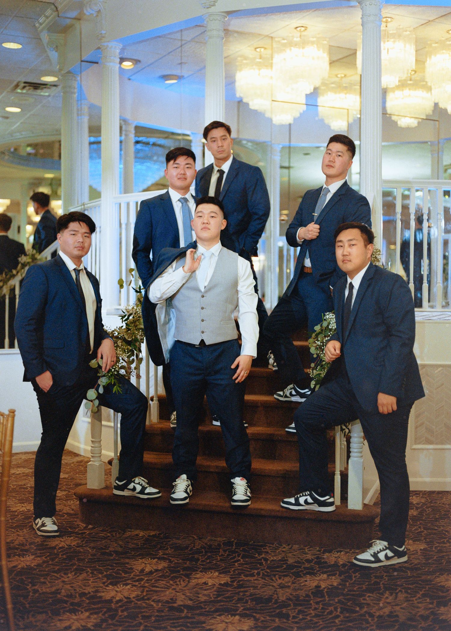 Groomsmen in navy suits and sneakers posing on grand staircase.