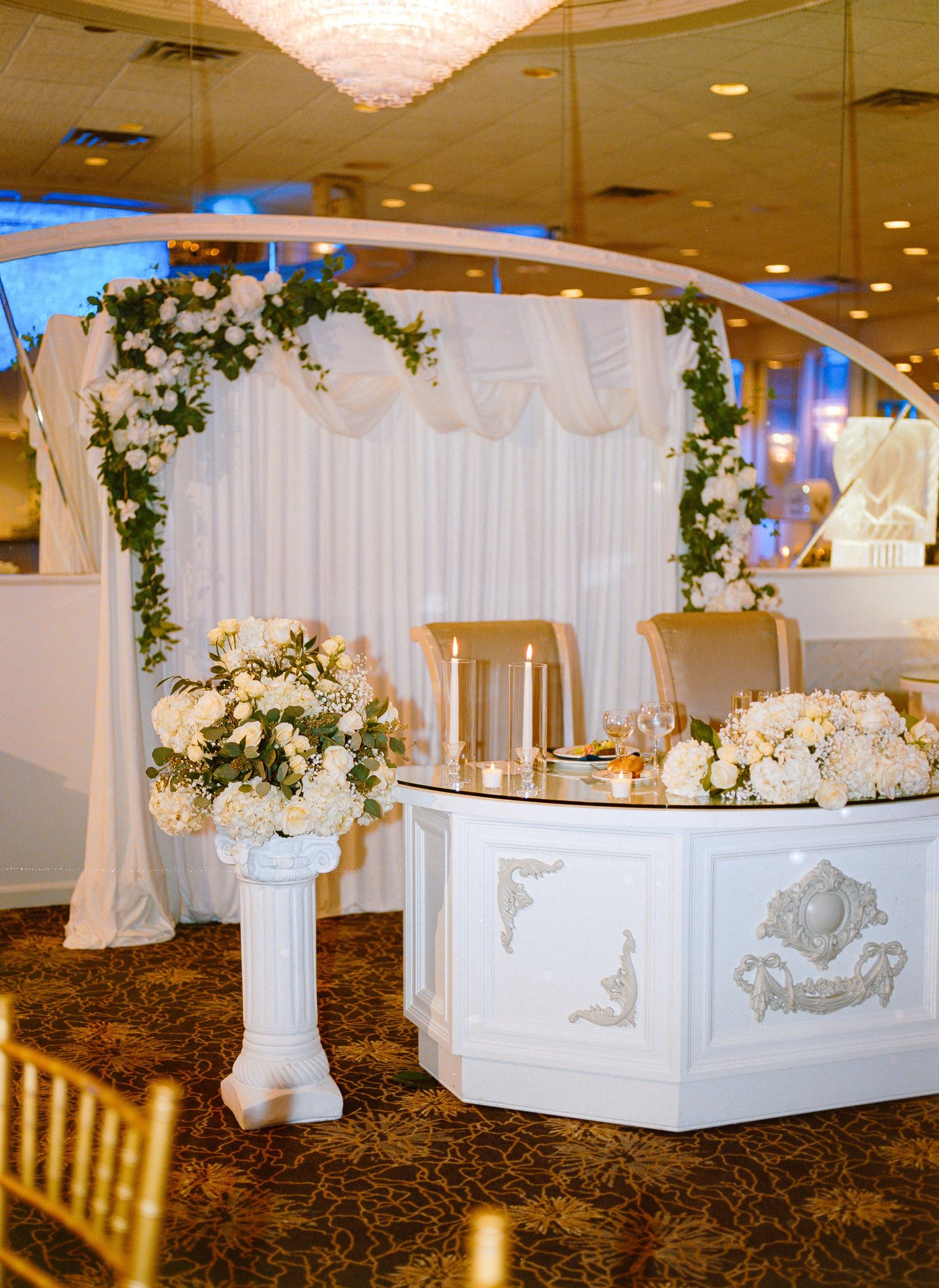 Elegant white wedding reception venue with floral decorations and draped fabric along the walls.