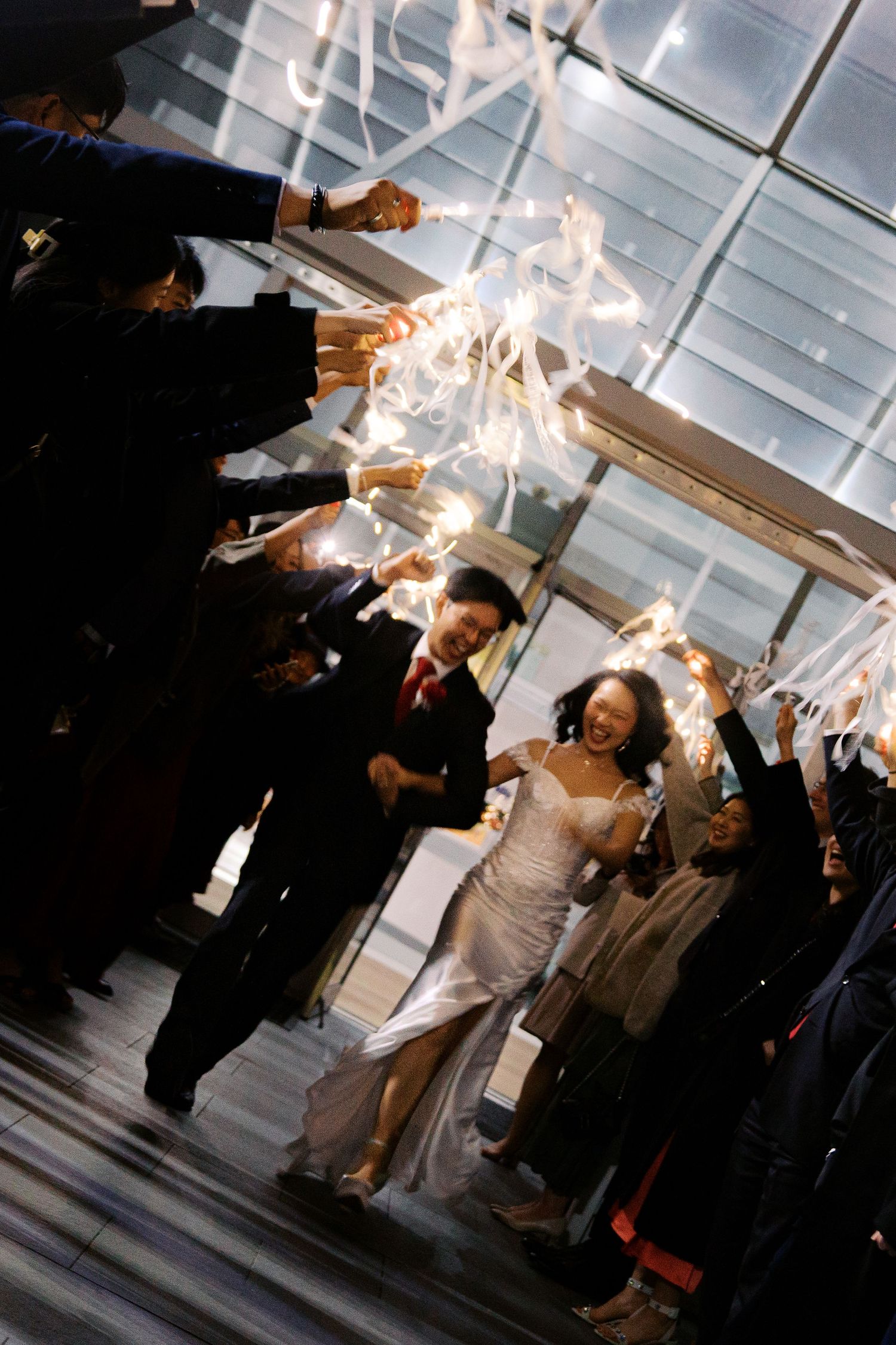 Wedding guests hold sparklers creating a glowing archway in a dimly lit venue.