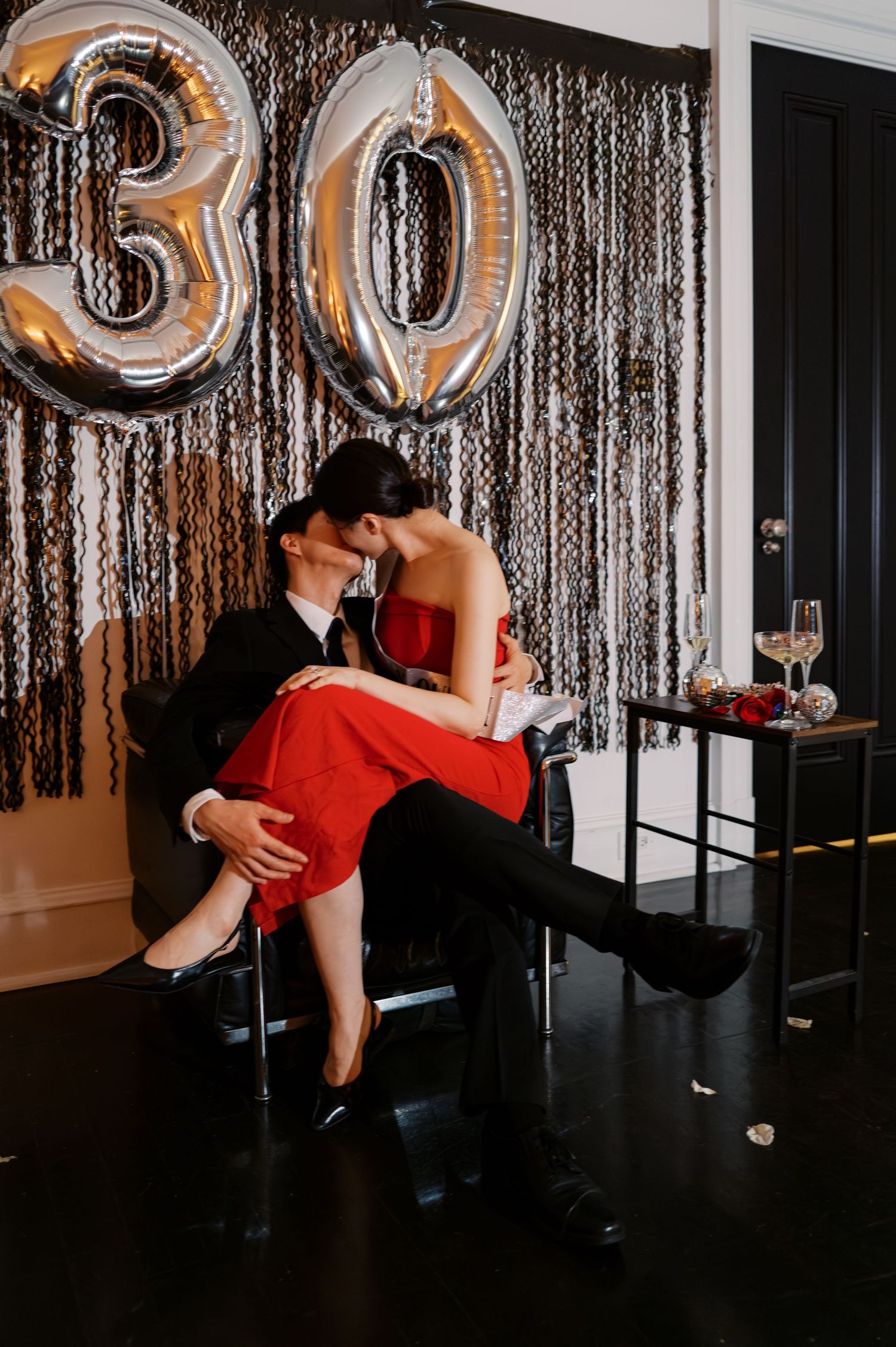 A dramatic dip pose in front of silver streamers and number balloons at a celebration.