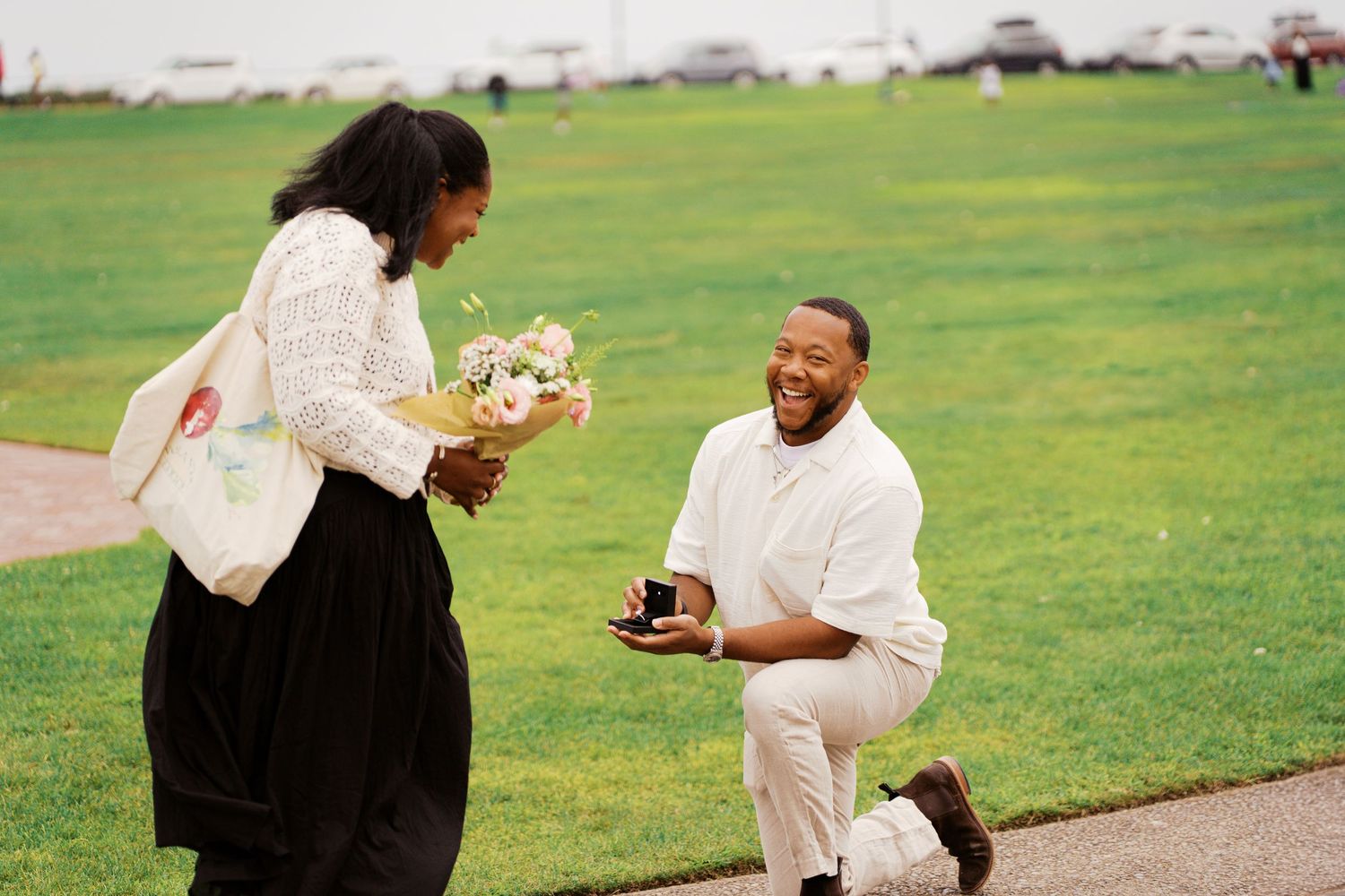 A surprise proposal moment on a lush green lawn with delicate flower bouquets.