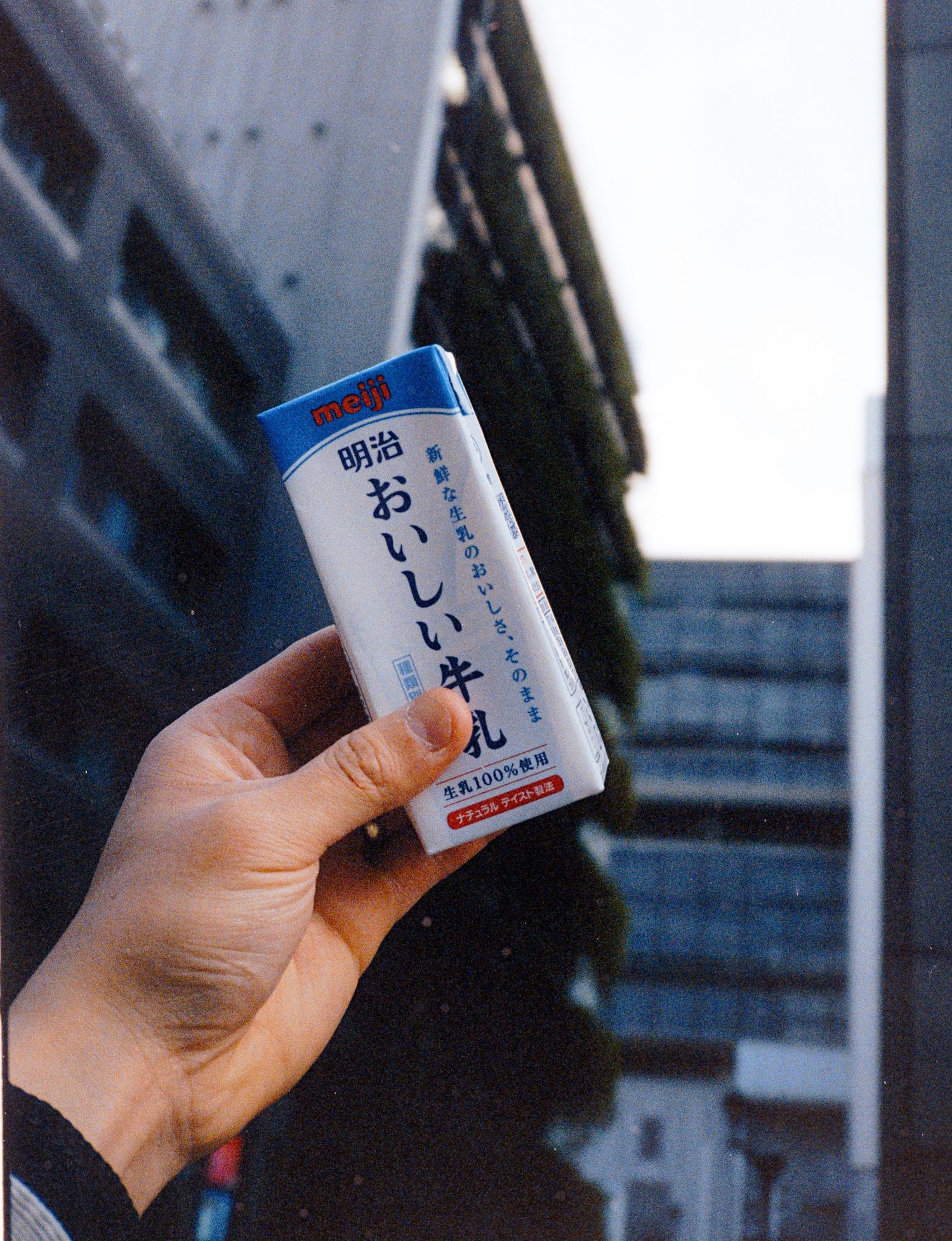 Hand holding a Japanese beverage can against an urban backdrop.