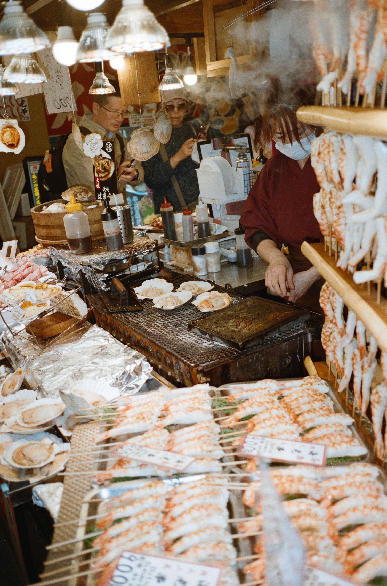 A busy Japanese street food stall with grills and hanging decorations serving customers.
