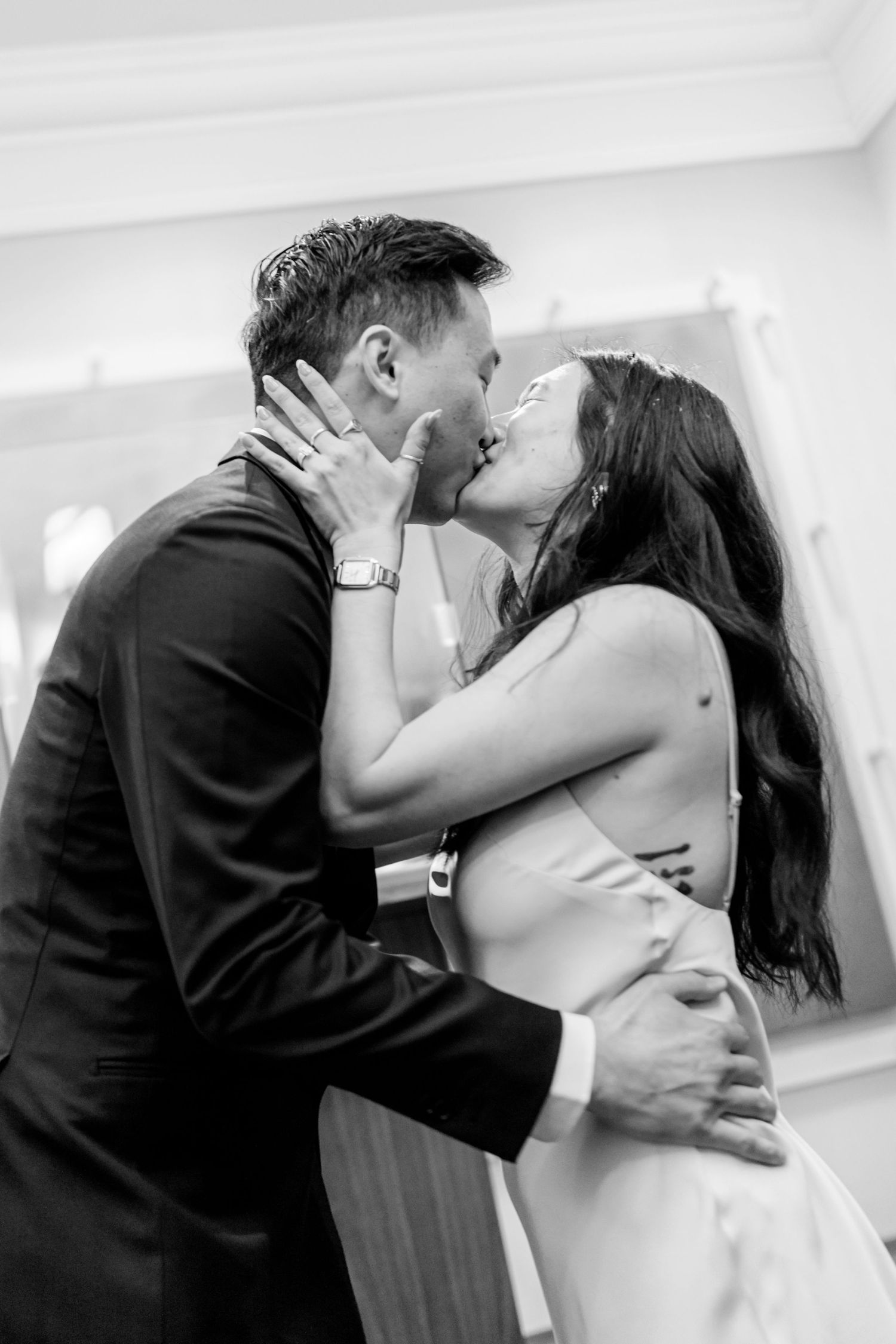 Black and white photo of a bride and groom sharing a romantic first kiss at their wedding ceremony.
