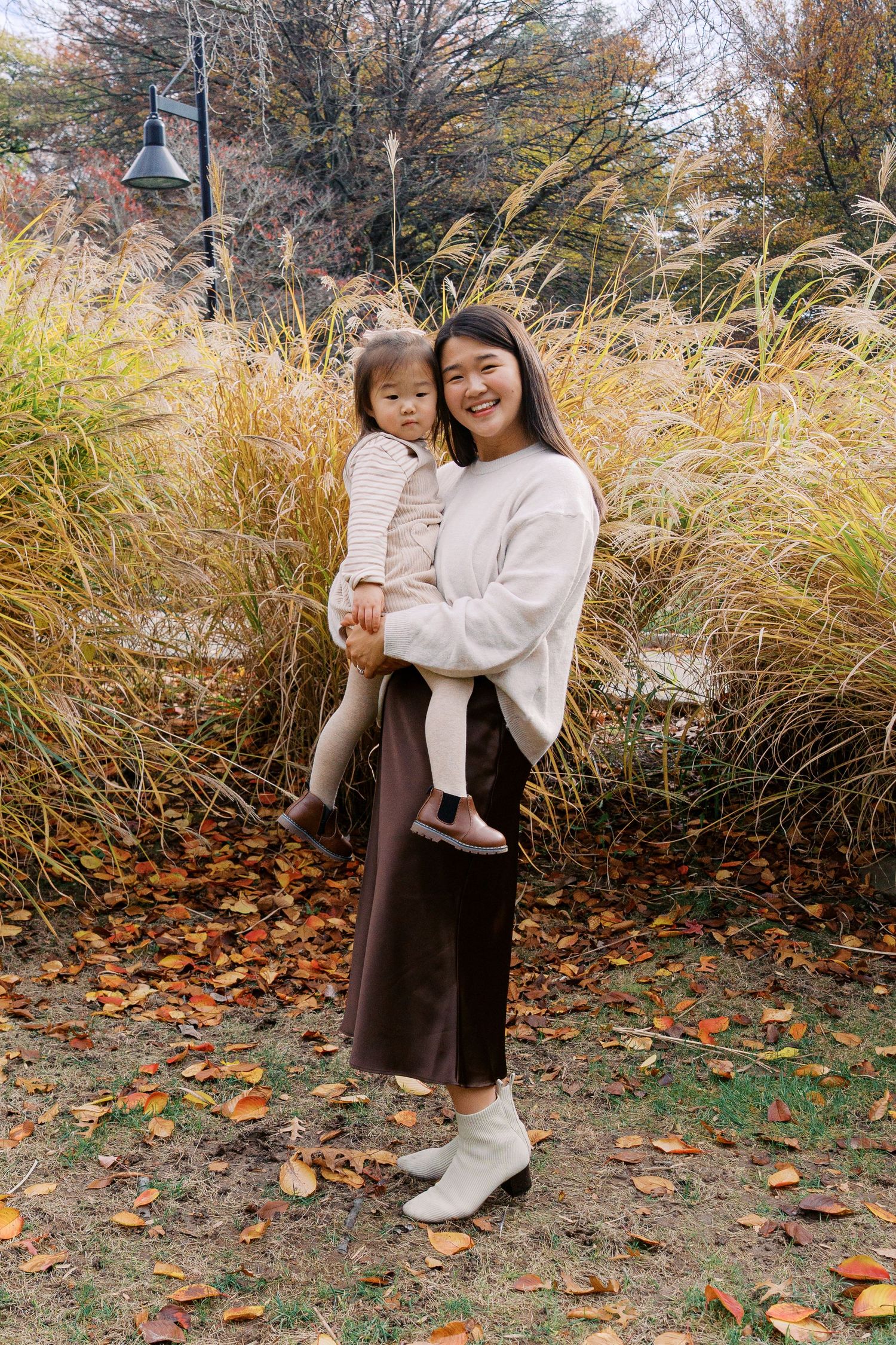 Mother and child standing together against tall ornamental grasses in autumn setting.