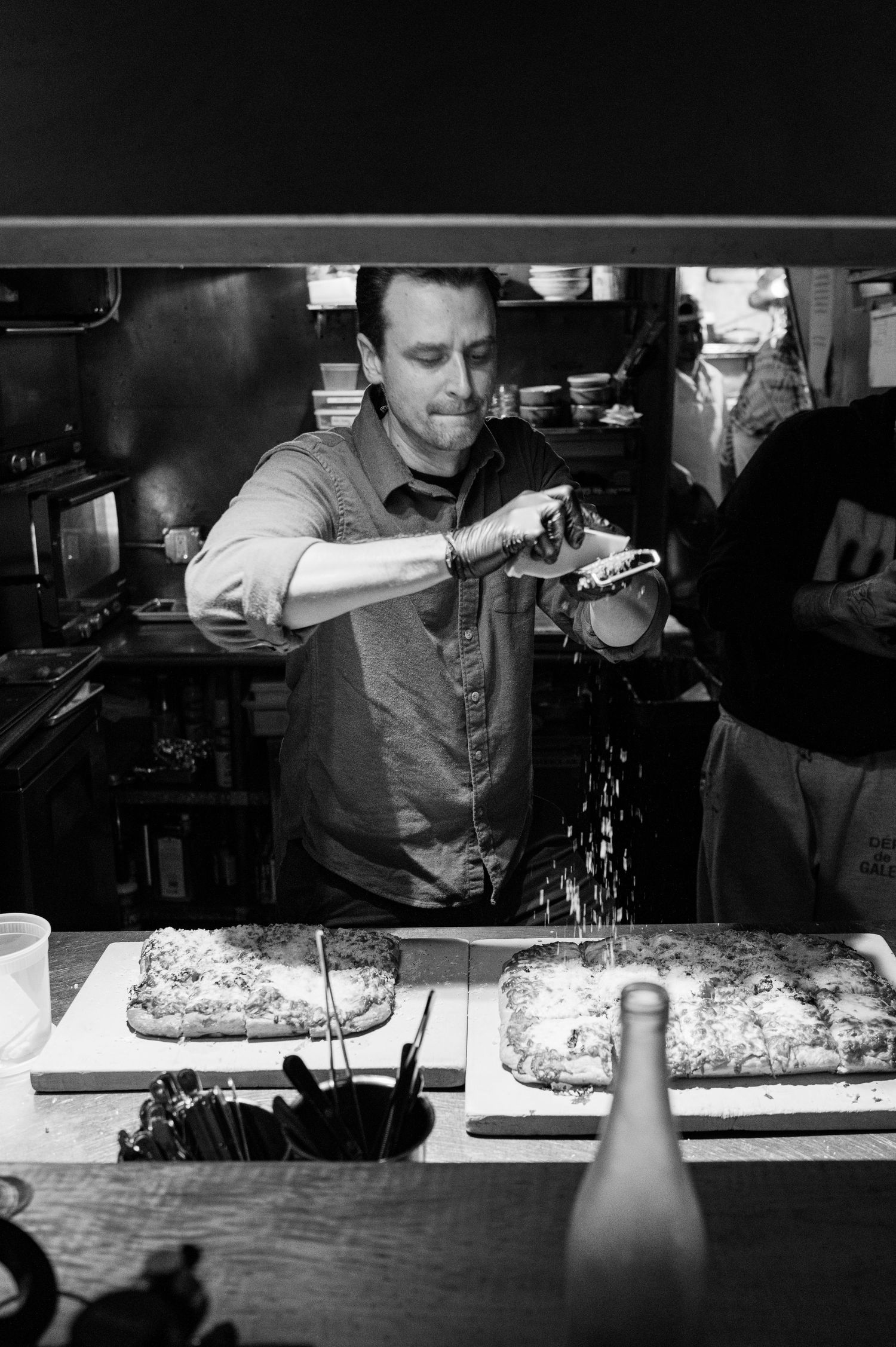 A chef in a kitchen uses a torch to finish a dish in black and white photography.