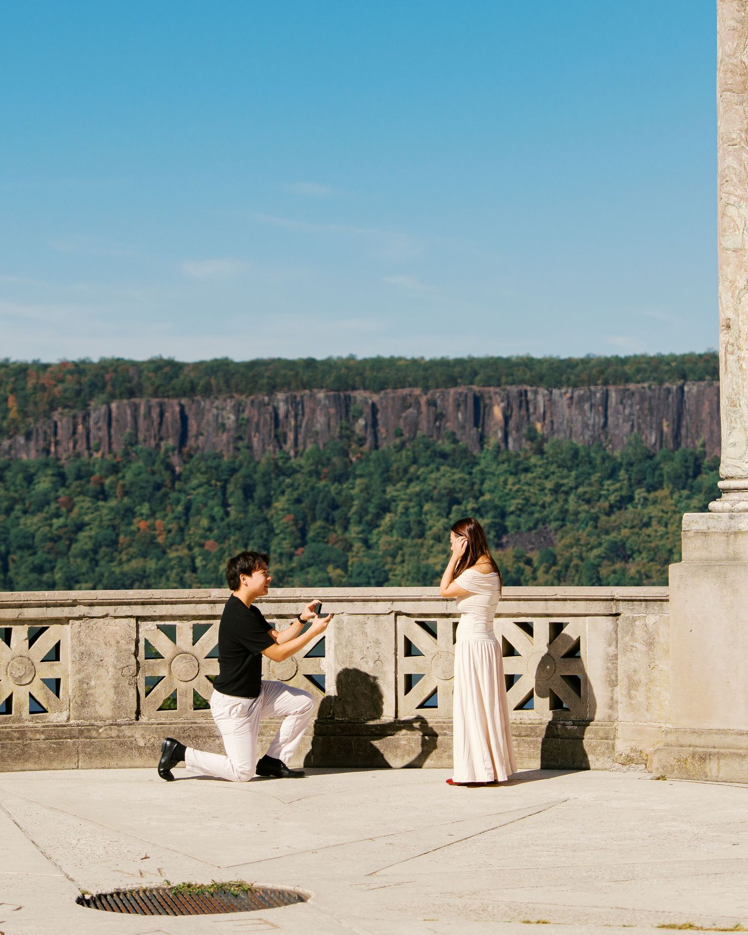A romantic proposal moment unfolds on a scenic stone balcony overlooking a dramatic cliff landscape.