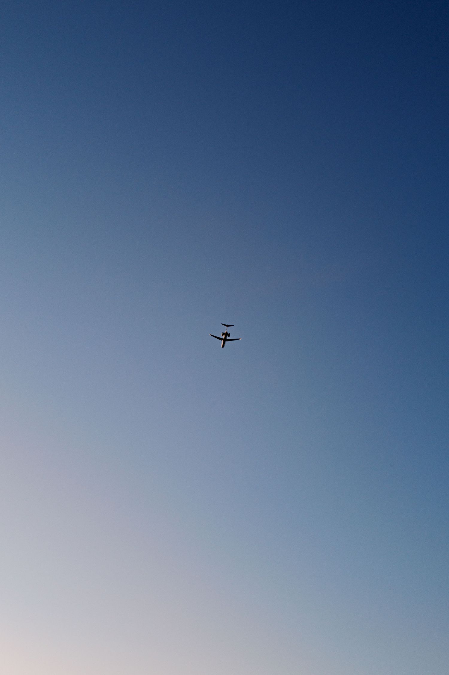 A small airplane silhouette flying high in a clear blue gradient sky during daytime.