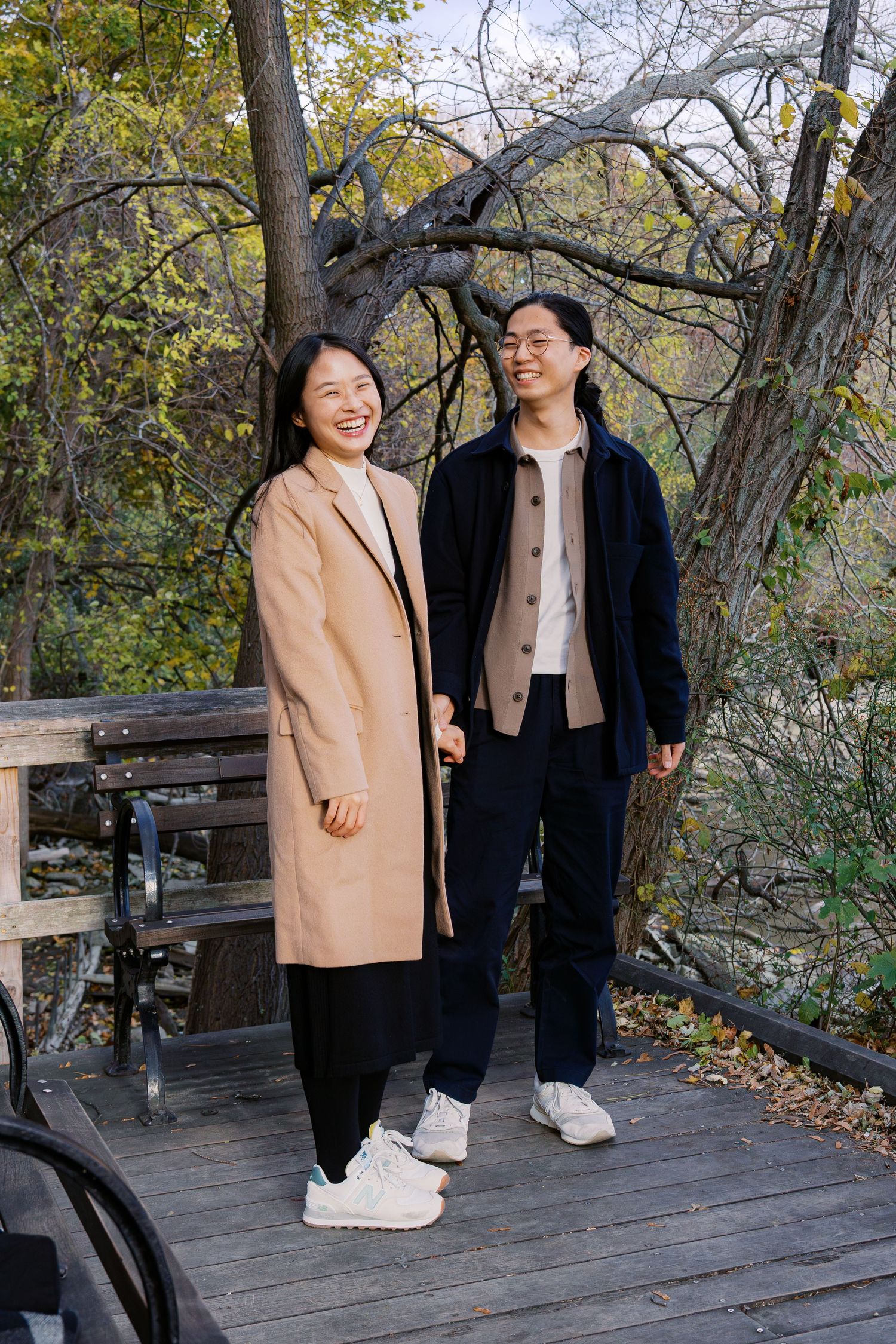 A couple shares joyful moments together while walking on a wooden deck surrounded by autumn trees.