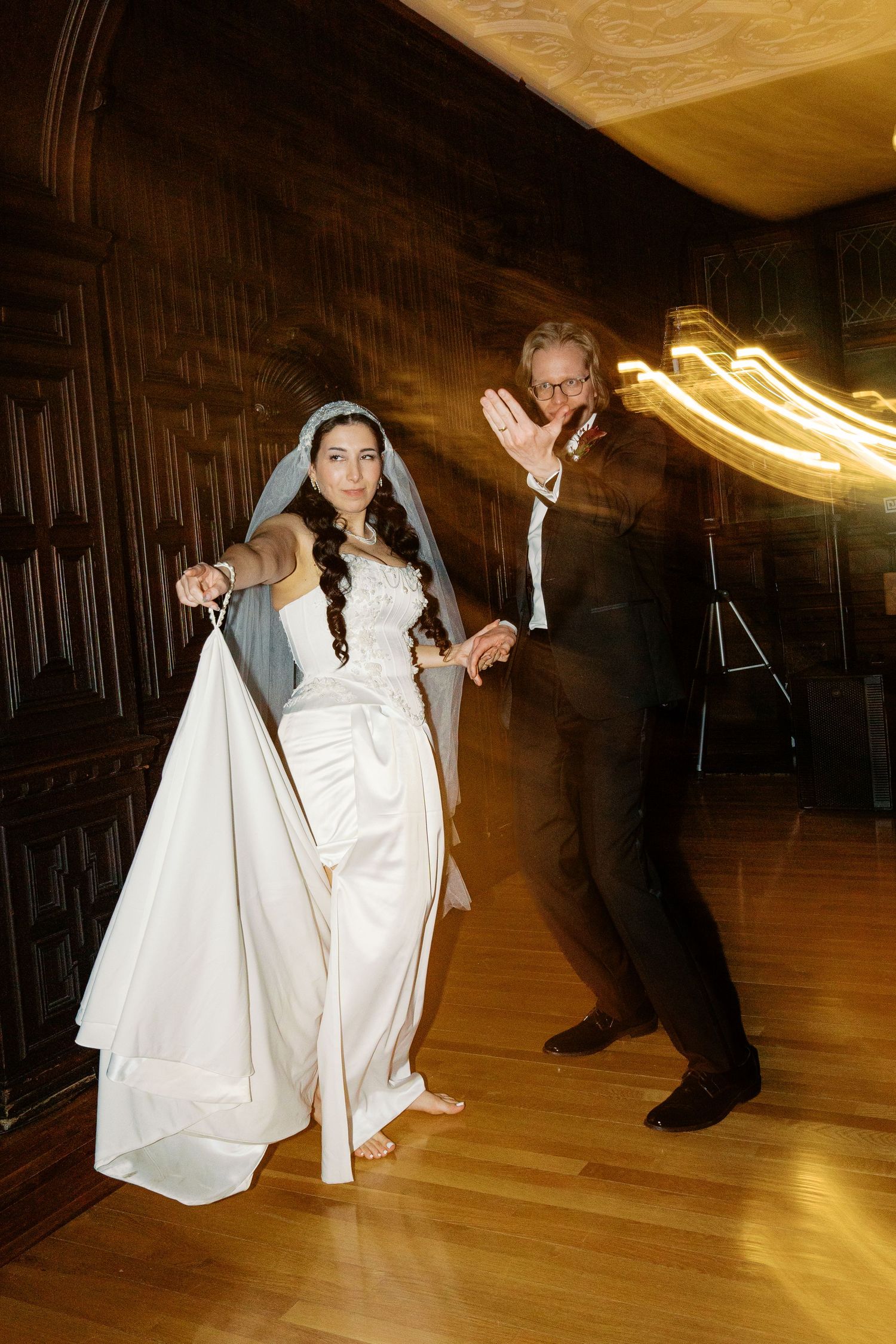 Wedding couple performs traditional dance moves on a wooden ballroom floor.